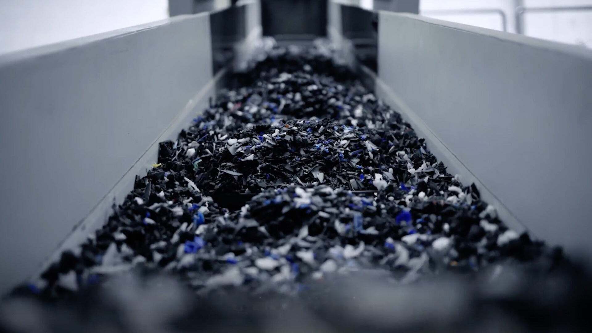 Schwarze und farbige Kunststoffstücke bewegen sich auf einem Förderband in einer industriellen Umgebung.