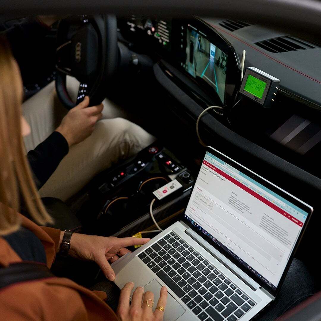 Sophia Schupritt sitzt mit einem Laptop auf dem Schoß auf dem Beifahrersitz eines Audis