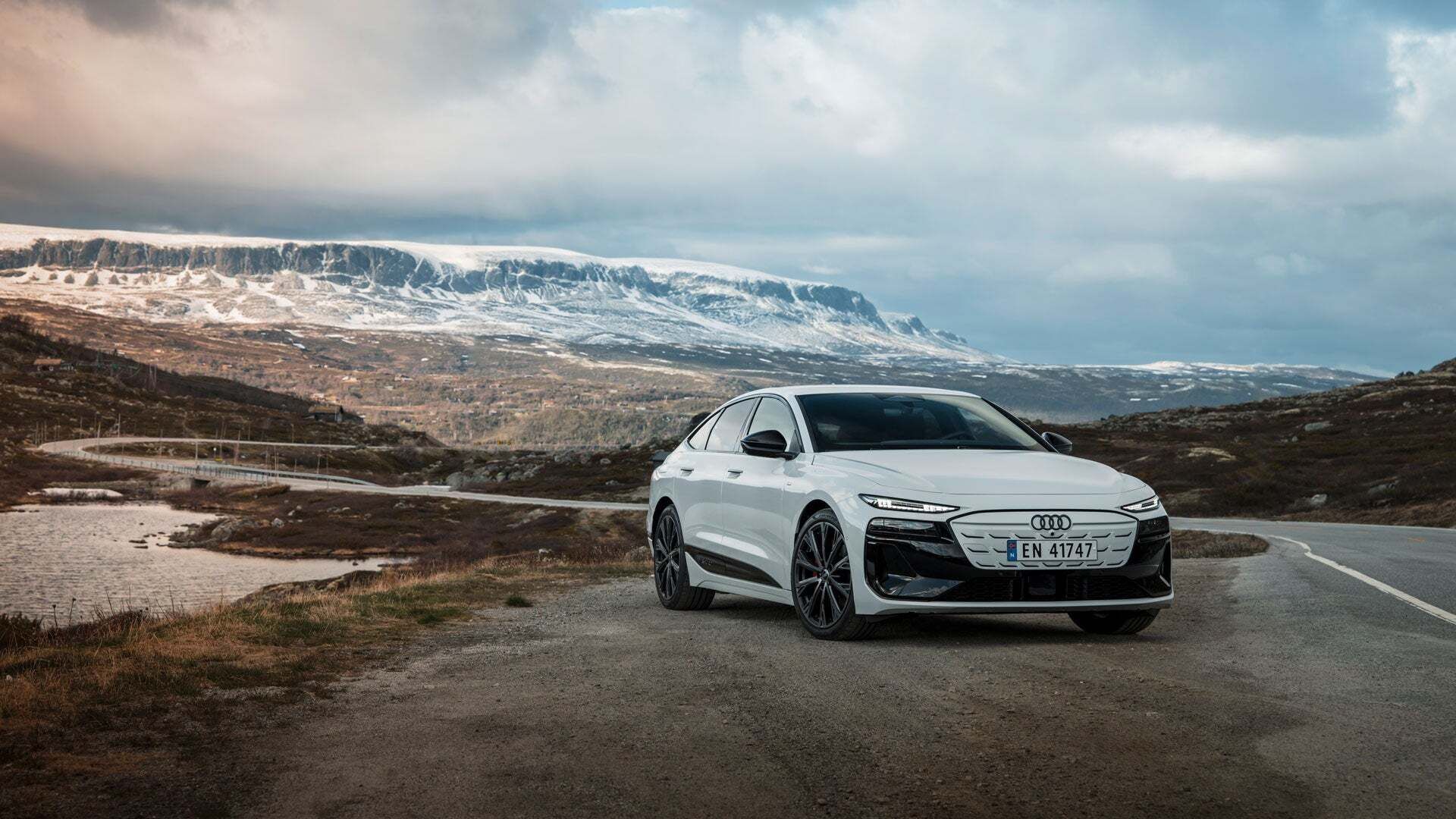 White Audi A6 Sportback e-tron in front of a Scandinavian natural backdrop with coniferous forests, snow-covered mountains and a river.
