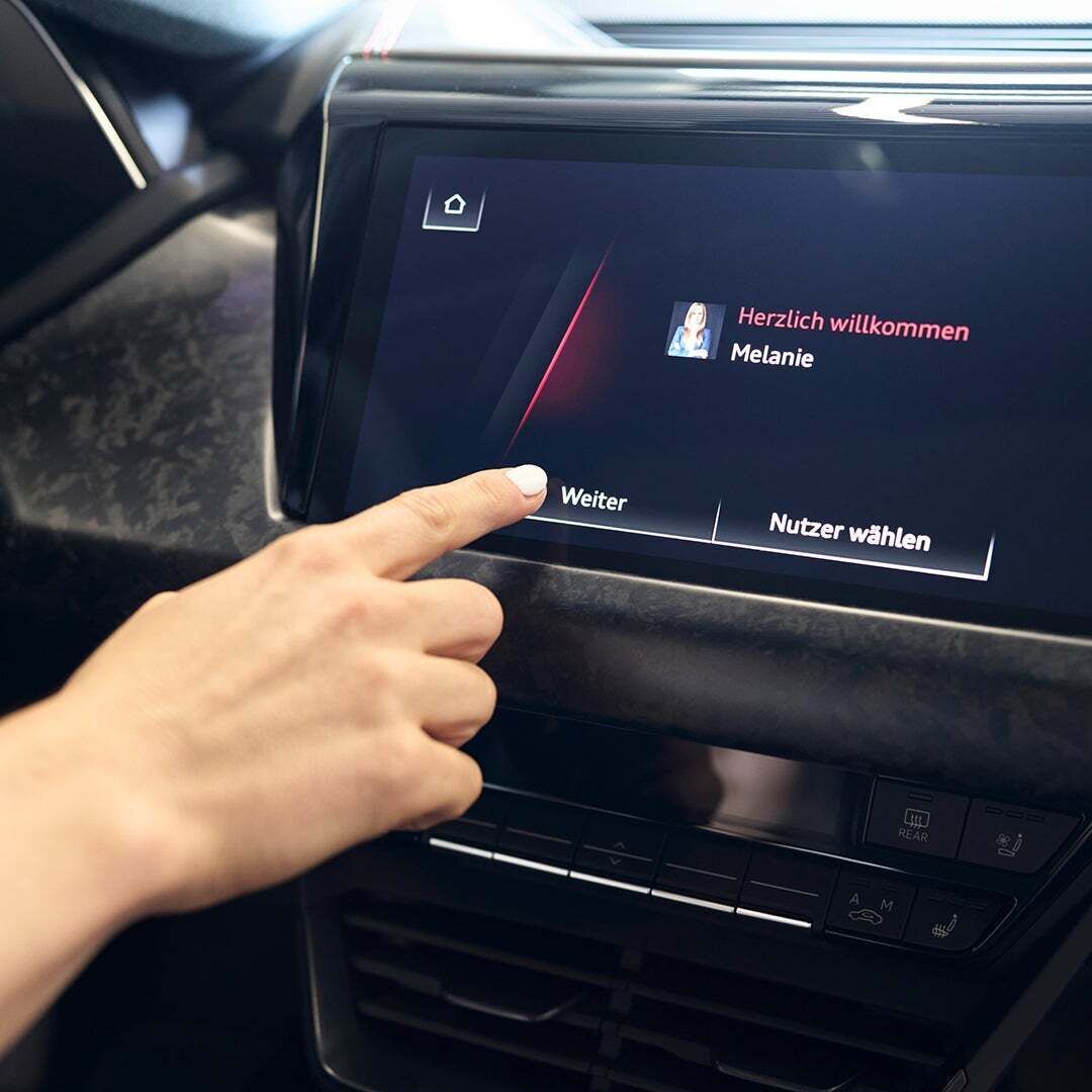 Eine Hand tippt auf den "Weiter" Button auf einem MMI-Display eines Audis