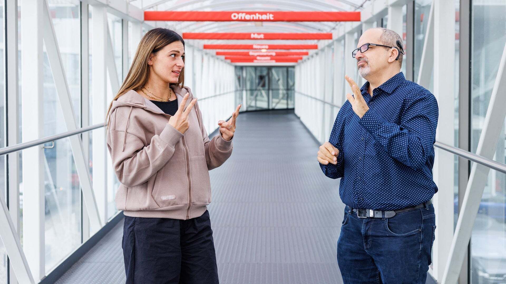 Vanessa is standing in a corridor next to her colleague Mathias, who is also deaf