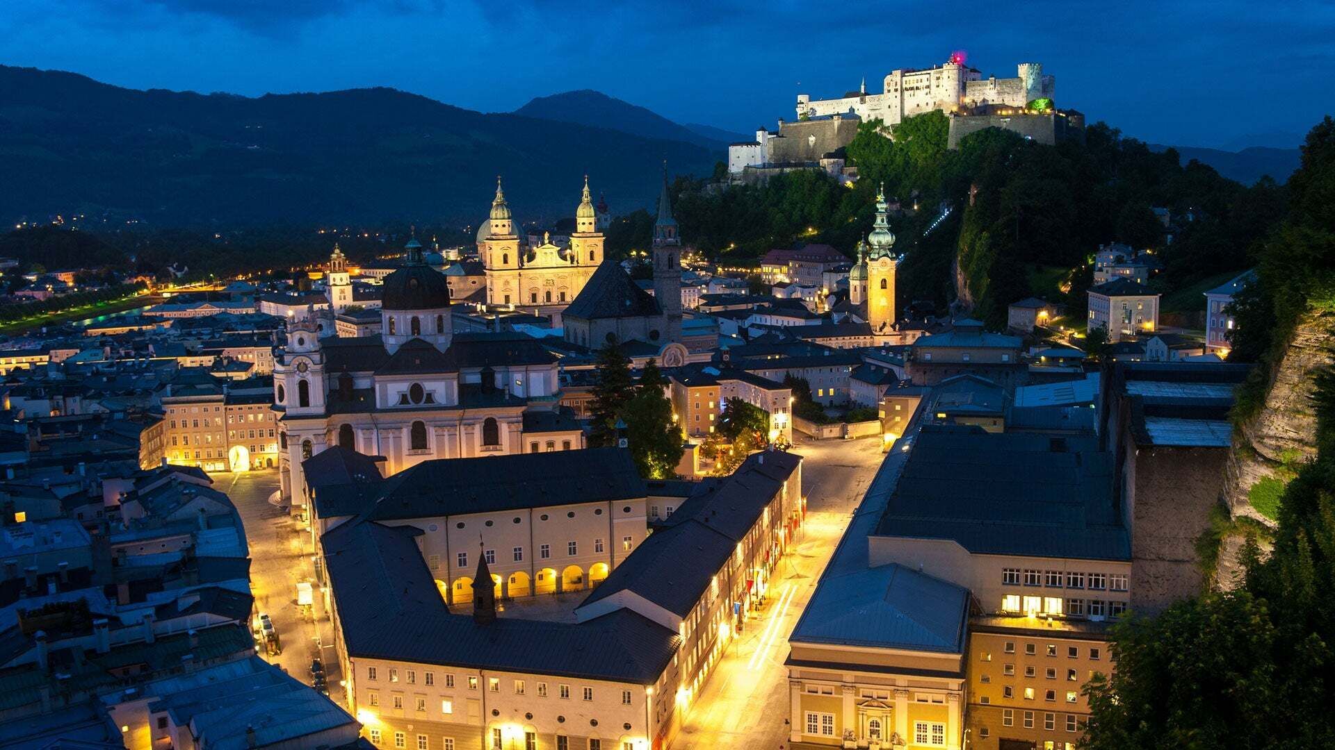 Abendliche Stadtansicht von Salzburg mit beleuchteter Altstadt und der Festung Hohensalzburg im Hintergrund.