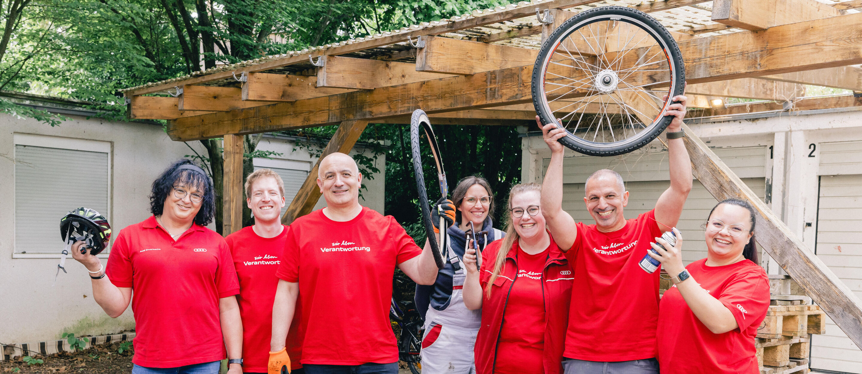 Employees in red T-shirts stand in front of a garage and hold bicycle parts in the air