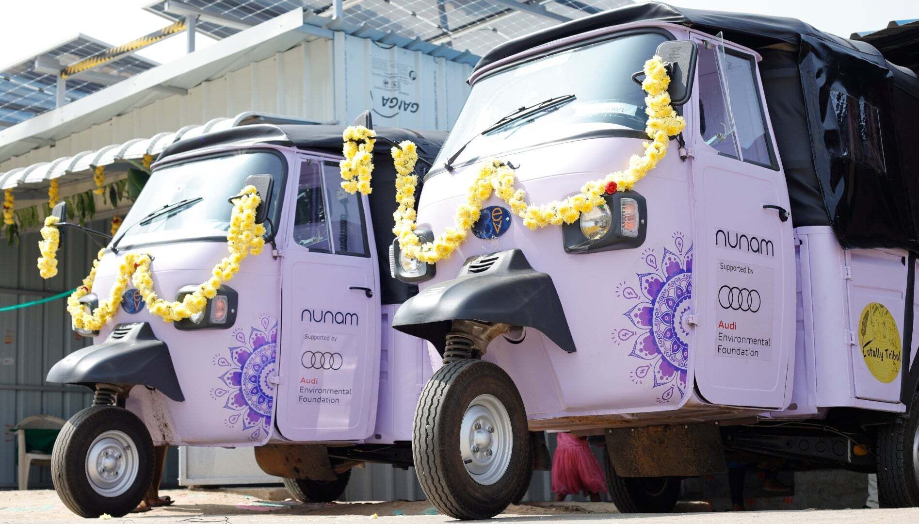 Two Nunam vehicles are parked in front of a building that has solar panels on its roof