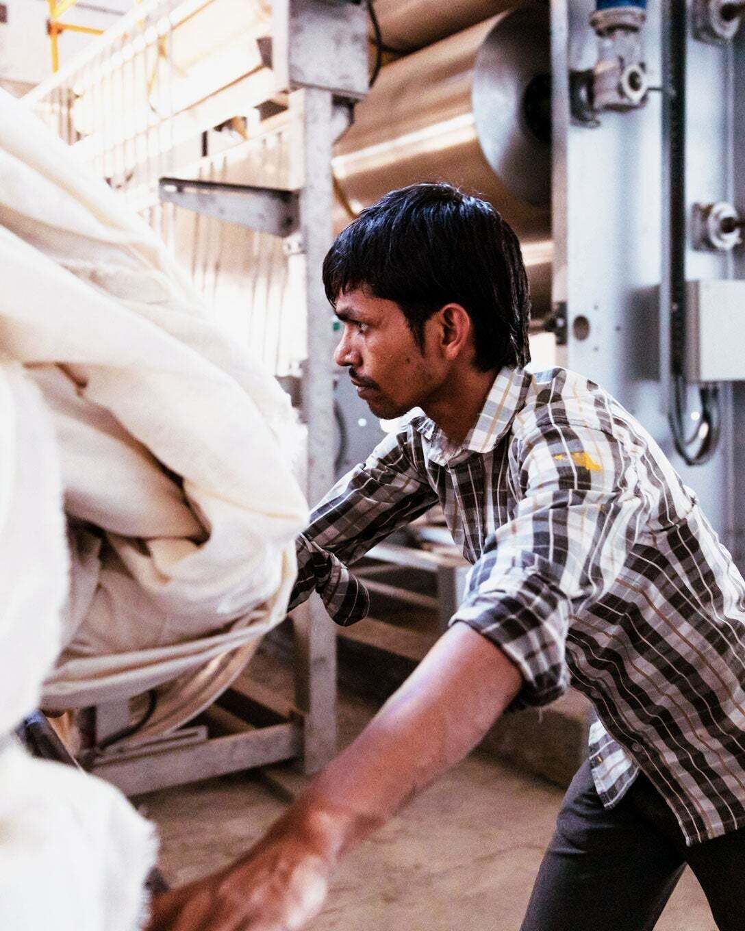 Man in a plaid shirt moves large lengths of fabric on a machine.