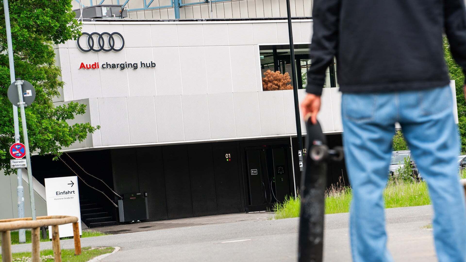 A man stands in front of the Audi charging hub with a skateboard in his hand