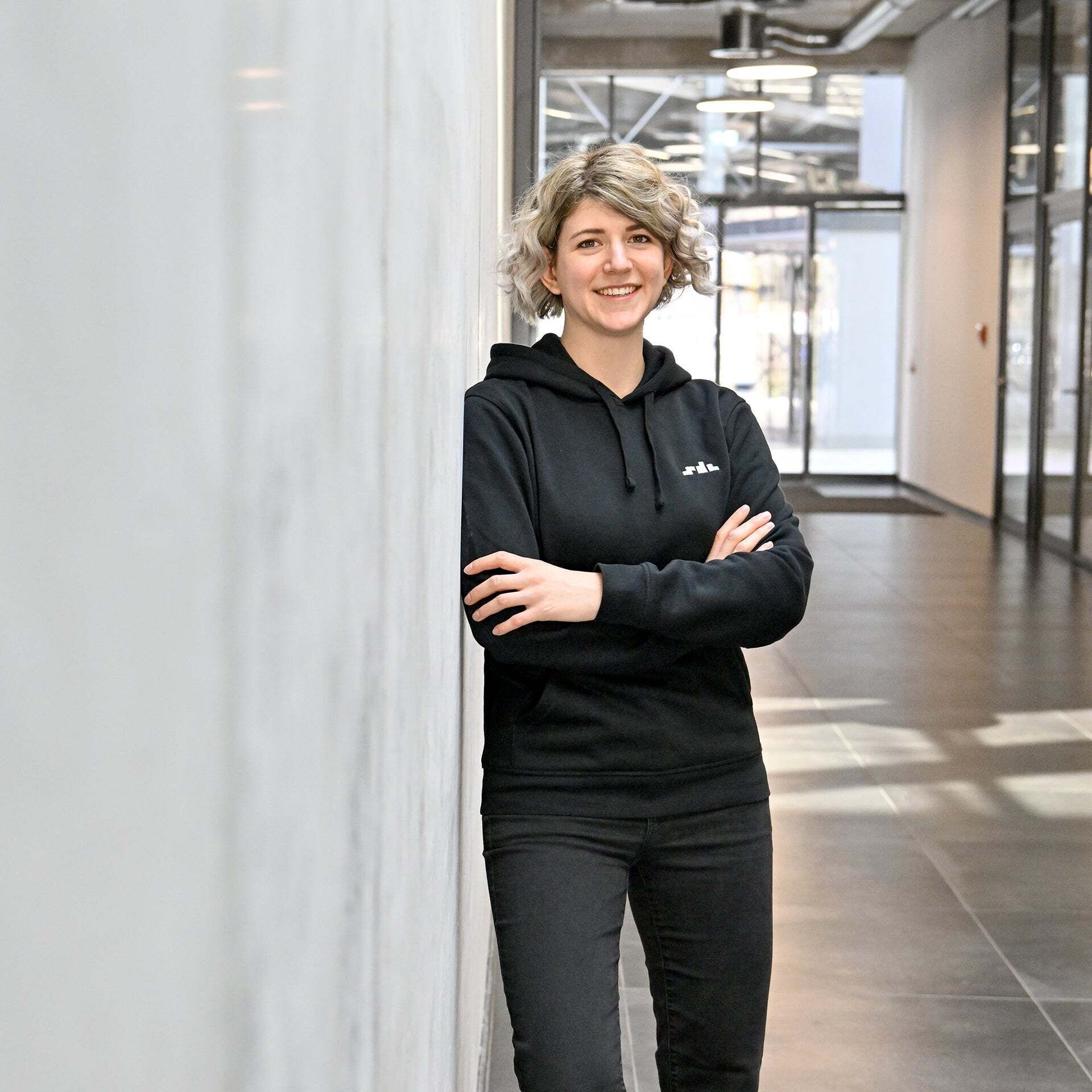 Nadine, Software Engineer SDC, leans against a wall and looks into the camera