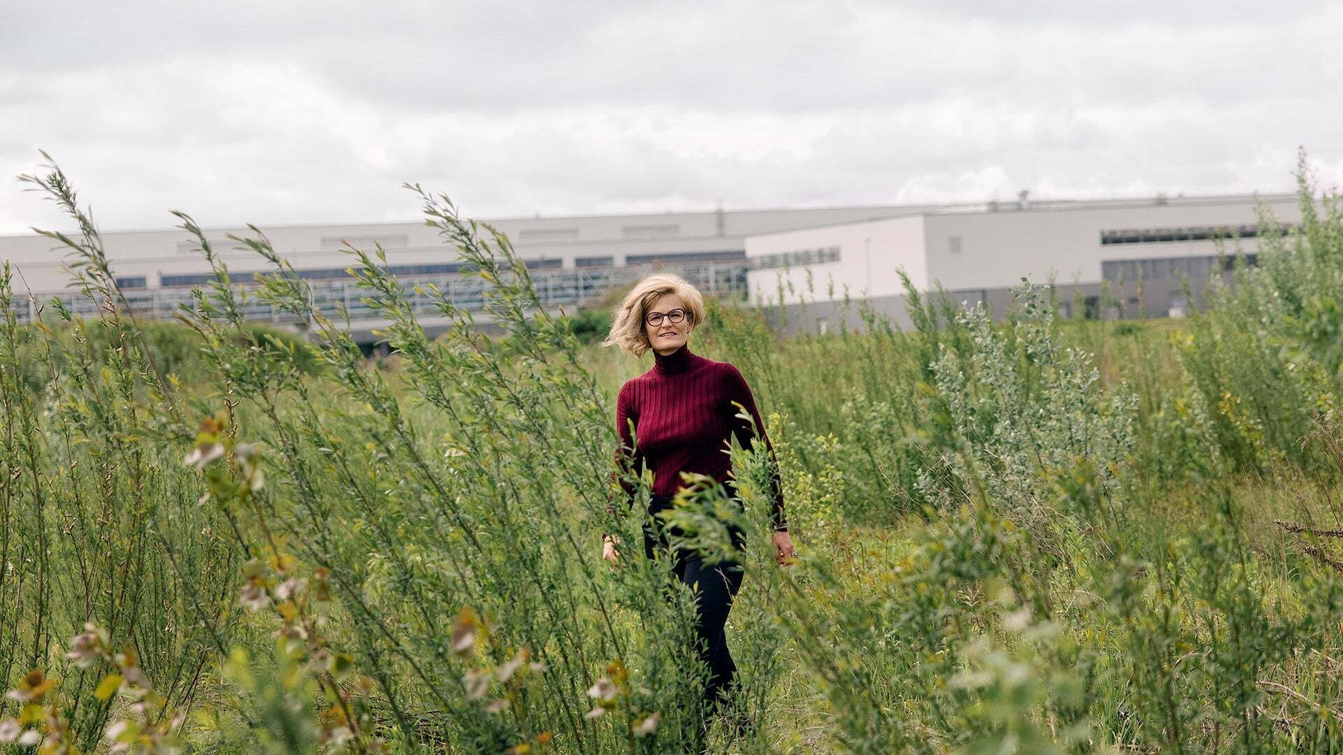 Dr. Antje Arnold stands in a flowering area and smiles, with a building in the background