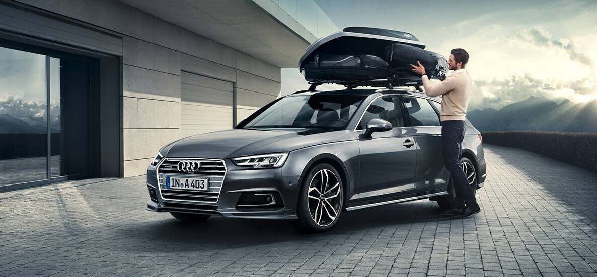 Grauer Audi A3, geparkt an einer Uferpromenade mit einer Brücke im Hintergrund und einem Schild mit der Aufschrift „RADIO PERMIT” darüber.