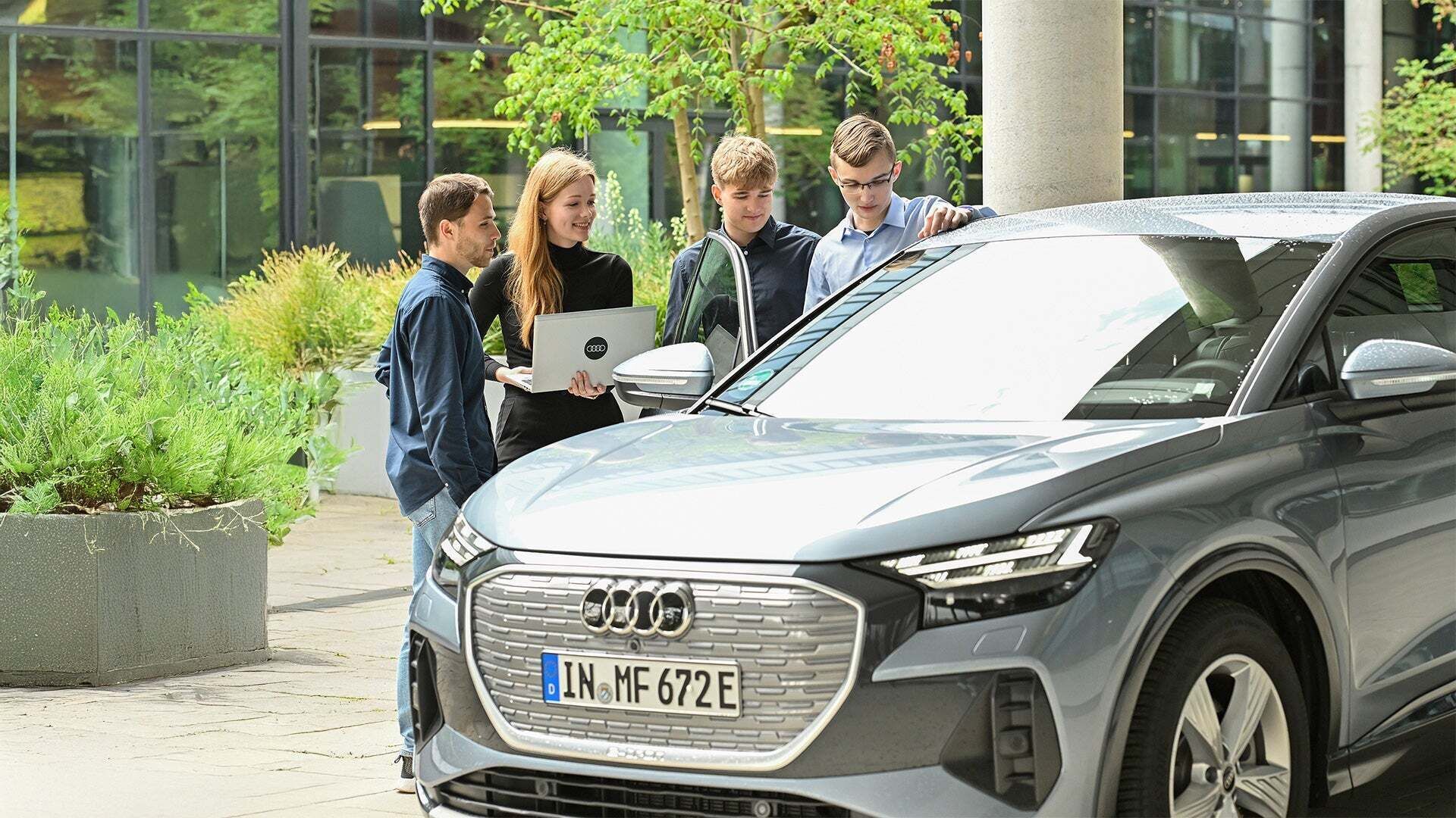 Ein paar Personen schauen sich einen Audi an, eine trägt einen Laptop