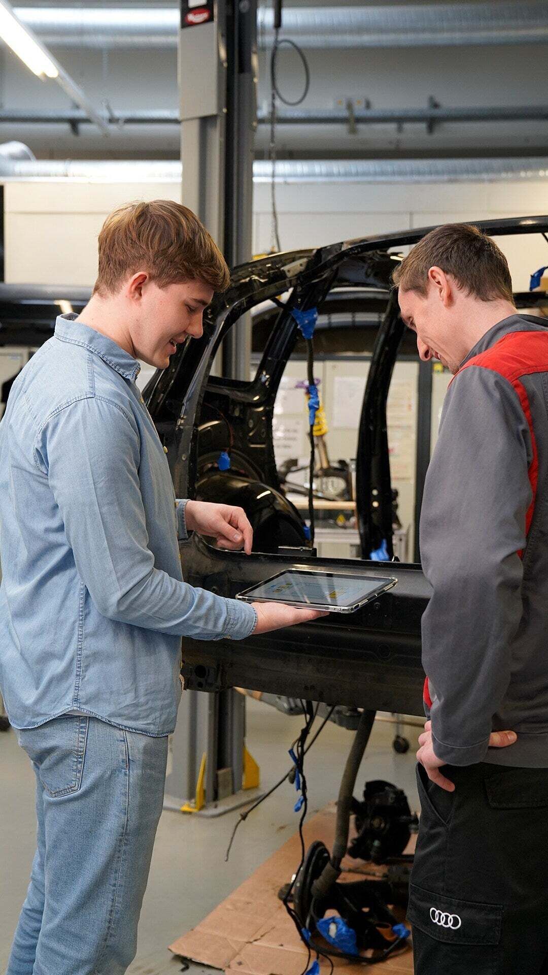 Zwei Auszubildende schauen sich etwas an der Karosserie eines Autos an