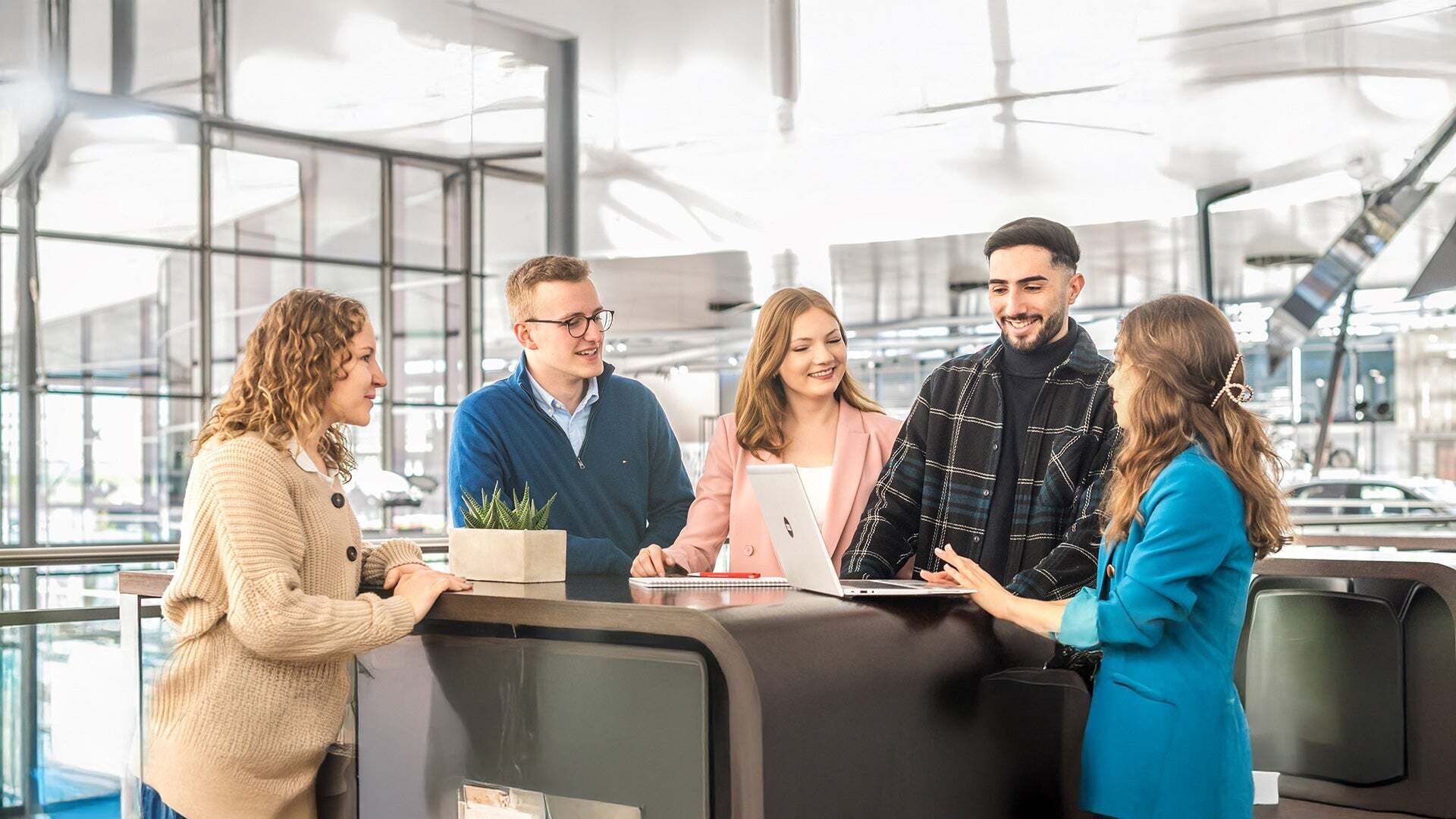 Gruppe von jungen Menschen, versammelt um einen Laptop an einem Stehtisch 