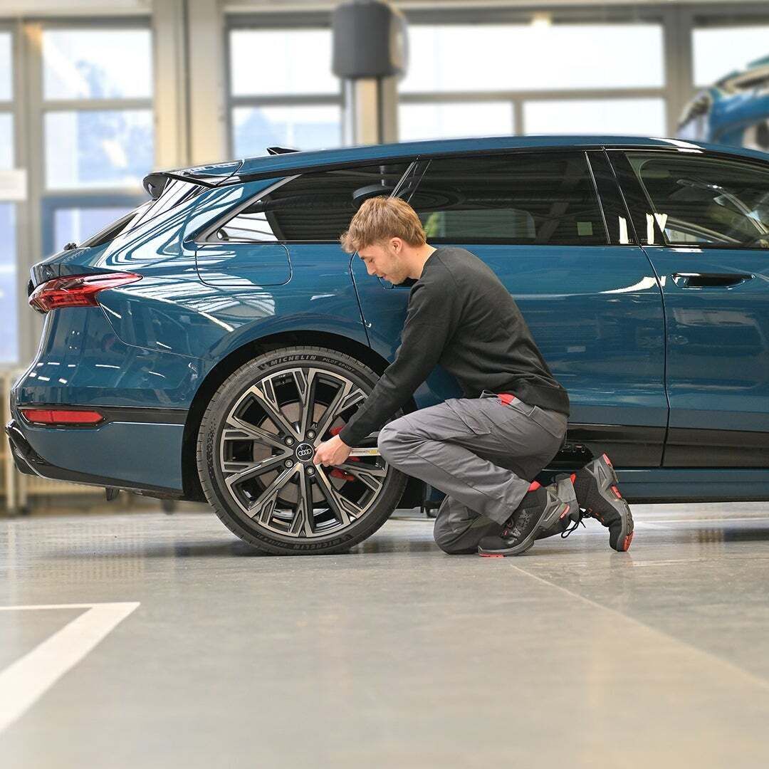 Julian kniet vor einem Hinterreifen eines blauen Audi