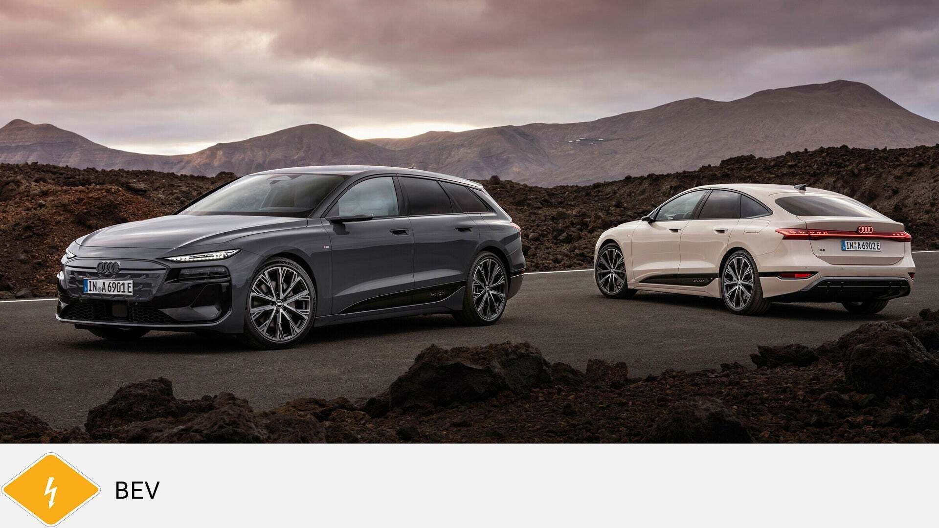 Zwei Audi A6 e-tron stehen auf Vulkanstraße vor Bergkulisse, grau und weiß. Unten gelbes BEV-Symbol mit Blitz.