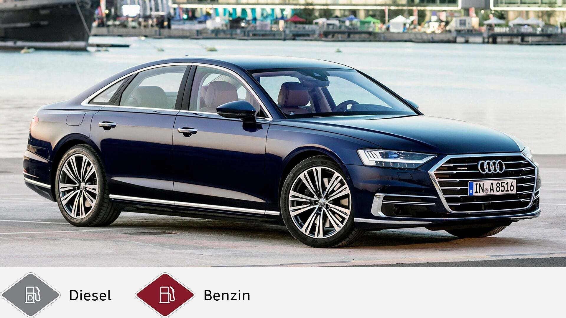 Blauer Audi A8 parkt seitlich an einem Hafenbecken mit Wasser und Gebäuden im Hintergrund. Unten graues Dieselsymbol und rotes Benzinsymbol.