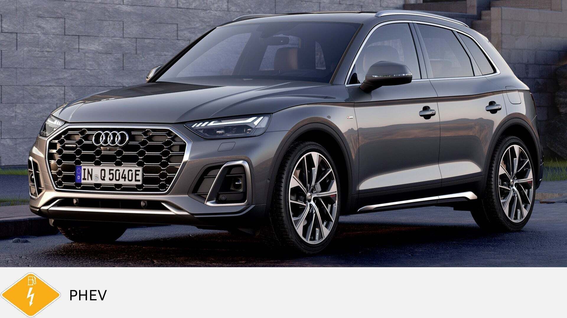 Grauer Audi Q5 TFSI e steht auf nasser Straße vor Steinmauer. Unten gelbes PHEV-Symbol mit Zapfsäule.