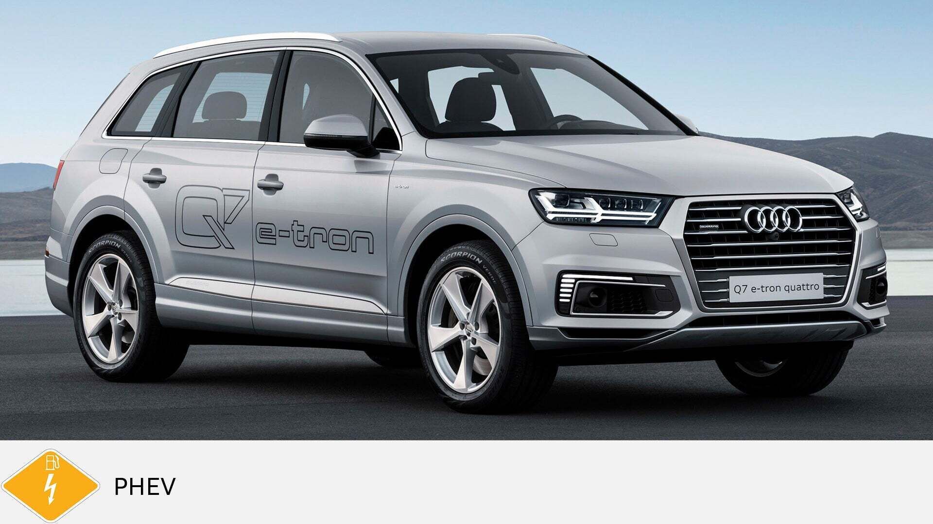 Silberner Audi Q7 e-tron quattro mit großem e-tron-Schriftzug steht am Wasser. Unten gelbes PHEV-Symbol mit Zapfsäule.