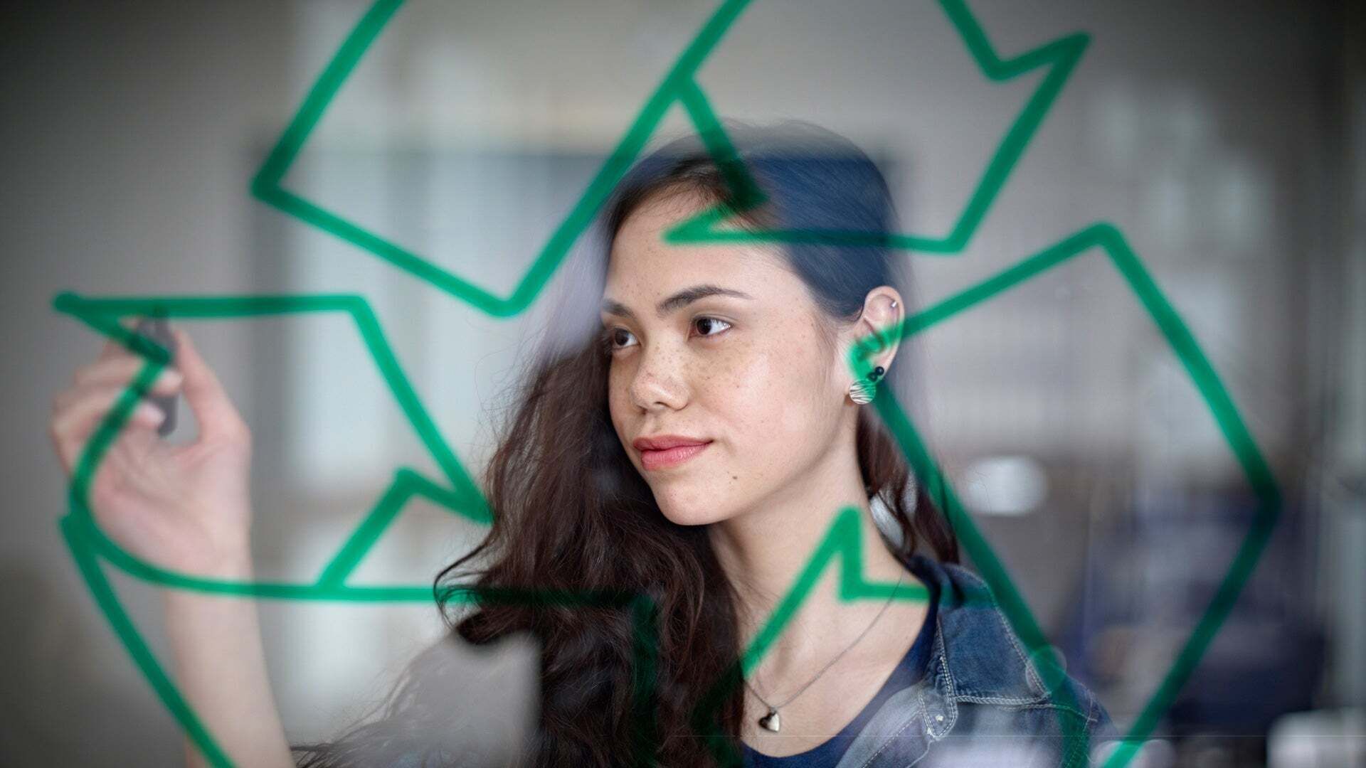 A young woman paints the recycling symbol, consisting of curved arrows arranged in a triangle, on a transparent board.