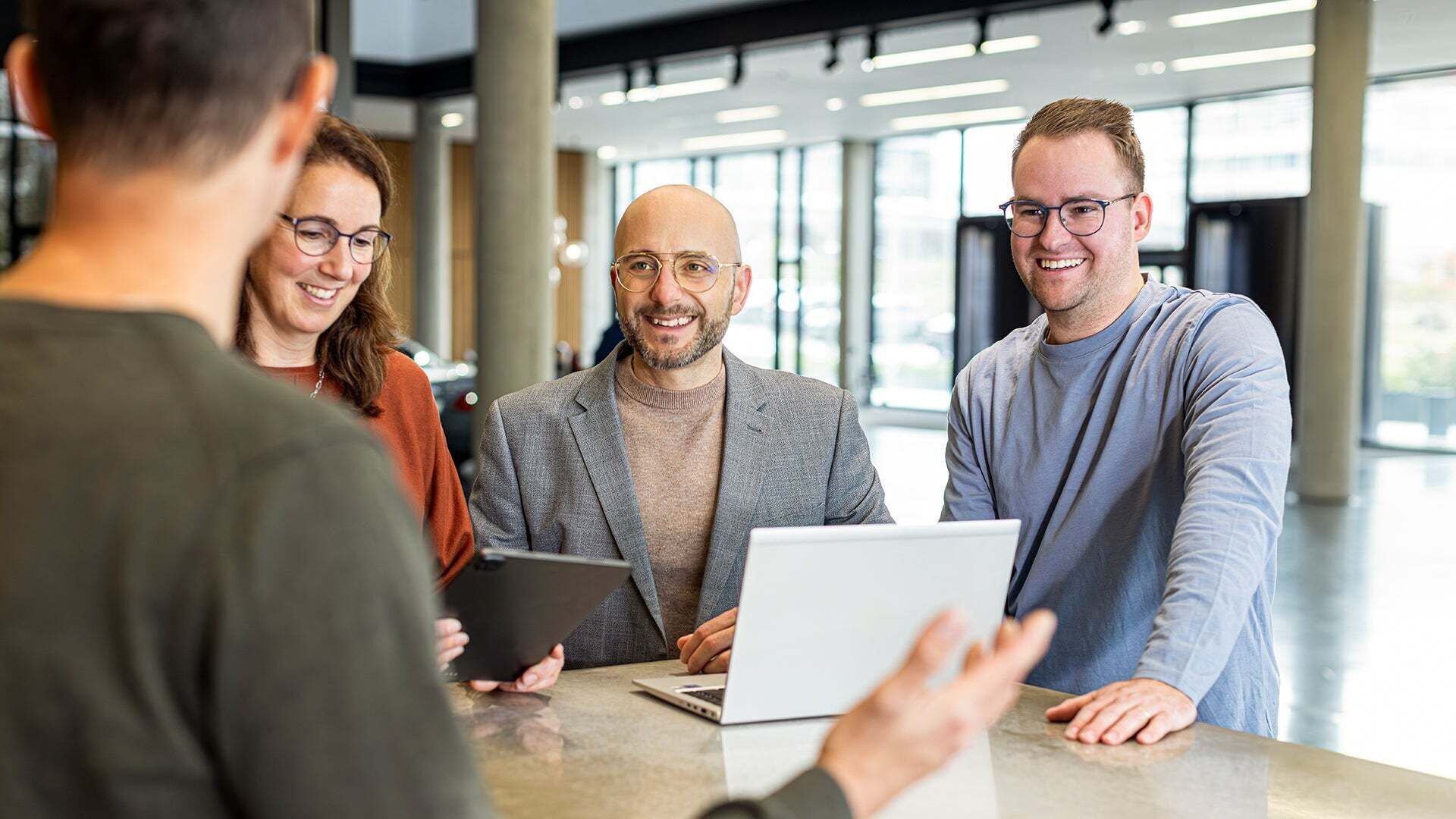 Mario De Felice steht mit ein paar Kollegen an einem Tisch worauf ein Laptop steht und lacht