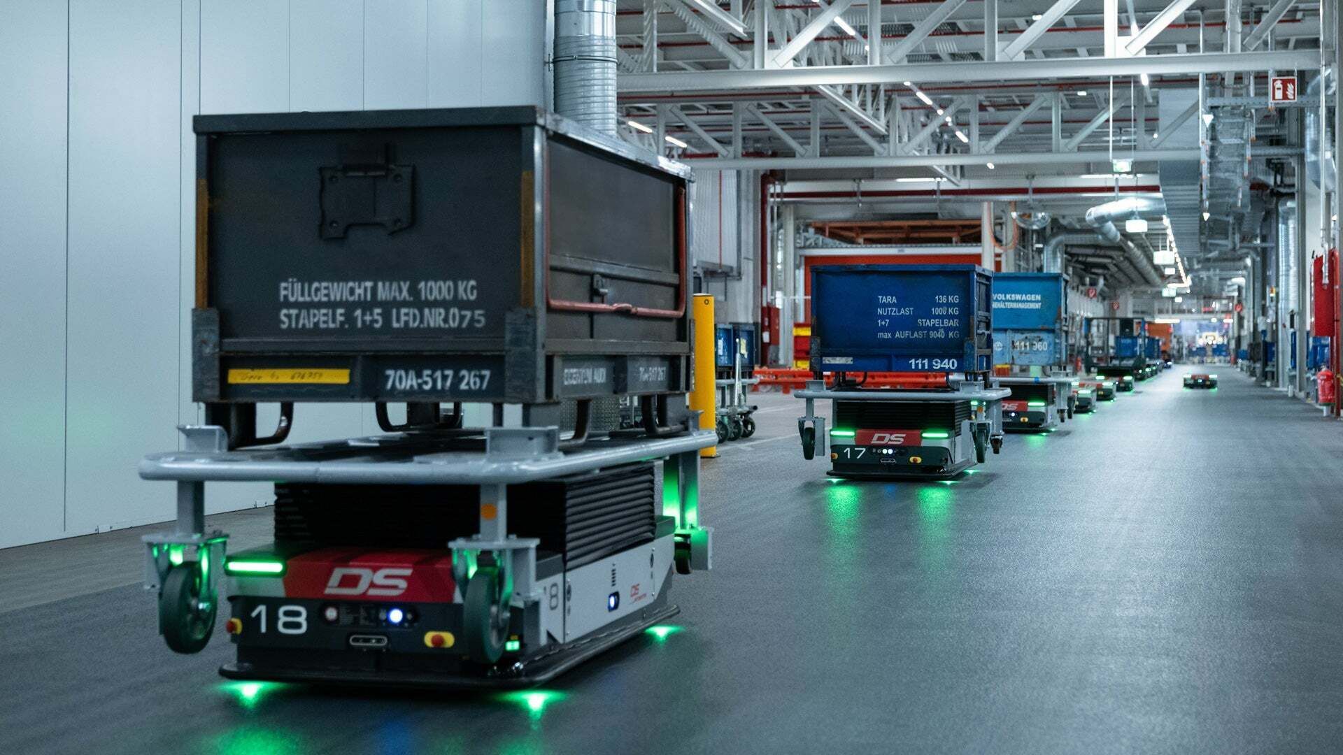 Driverless transport vehicles drive crates in a long line through a production hall to their destination.