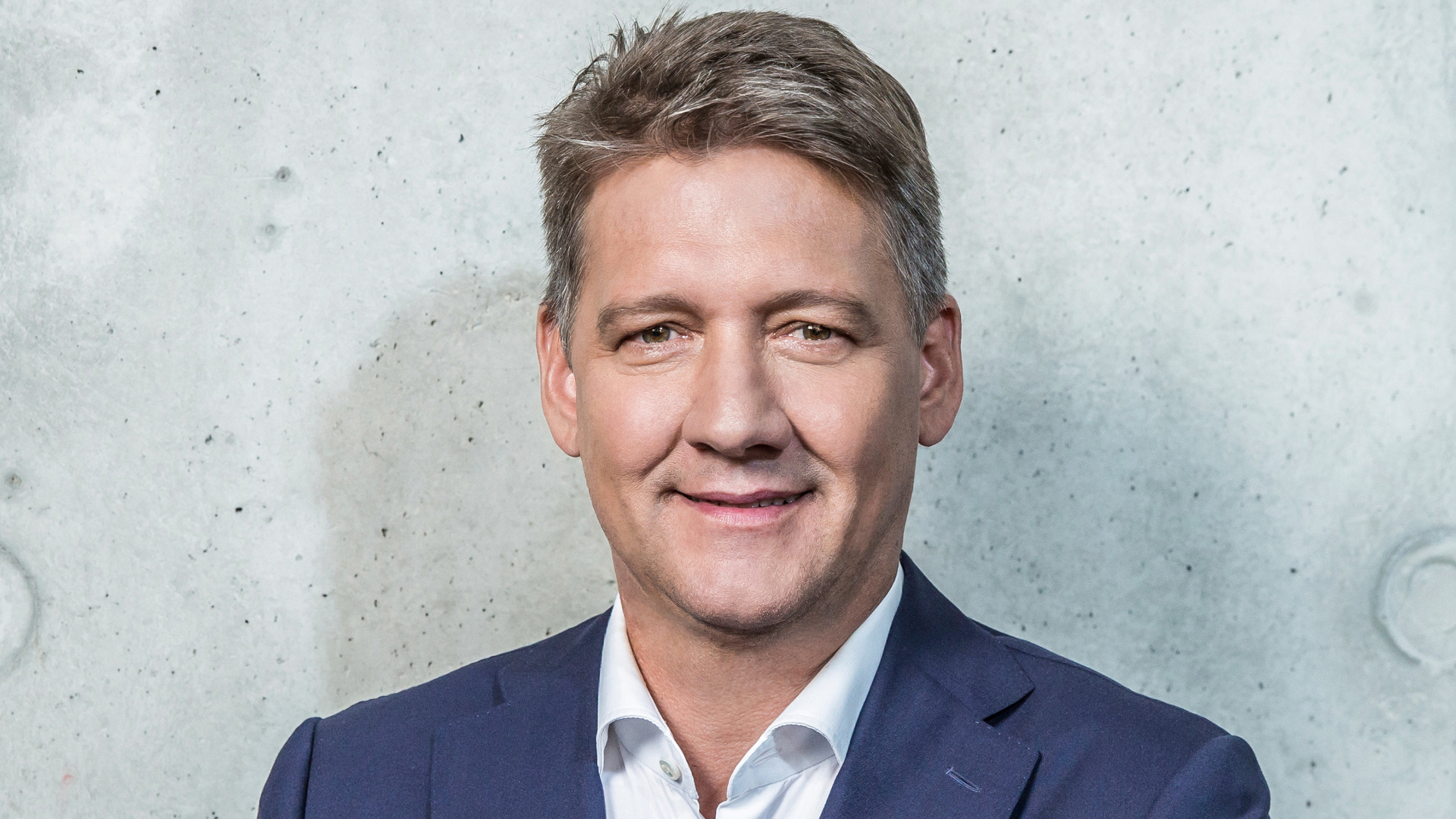 Portrait photo of CEO Gernot Döllner in front of a light stone wall.