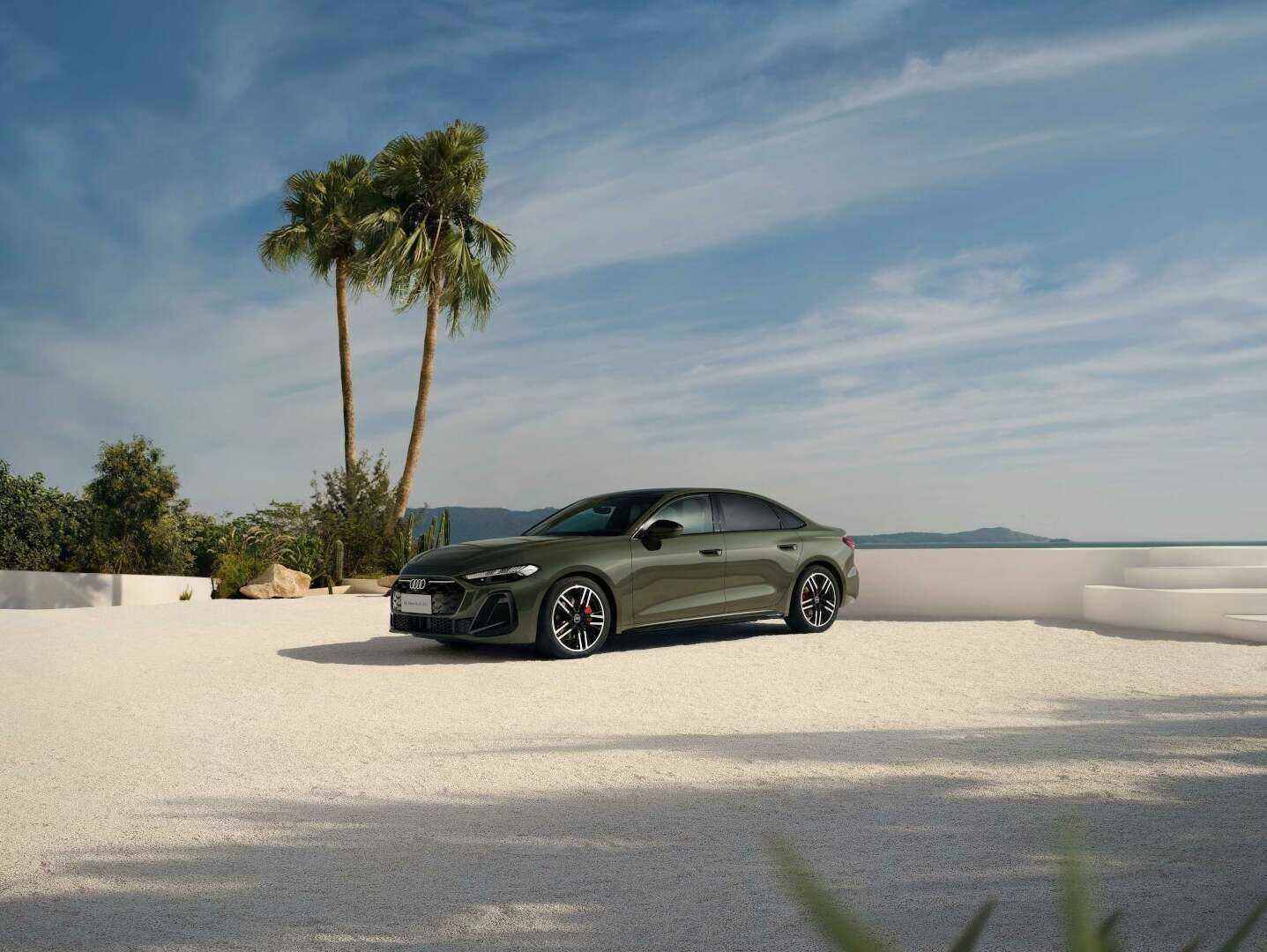 A green Audi A5L is parked on a bright terrace with palm trees, an open sky, and a view of the sea.