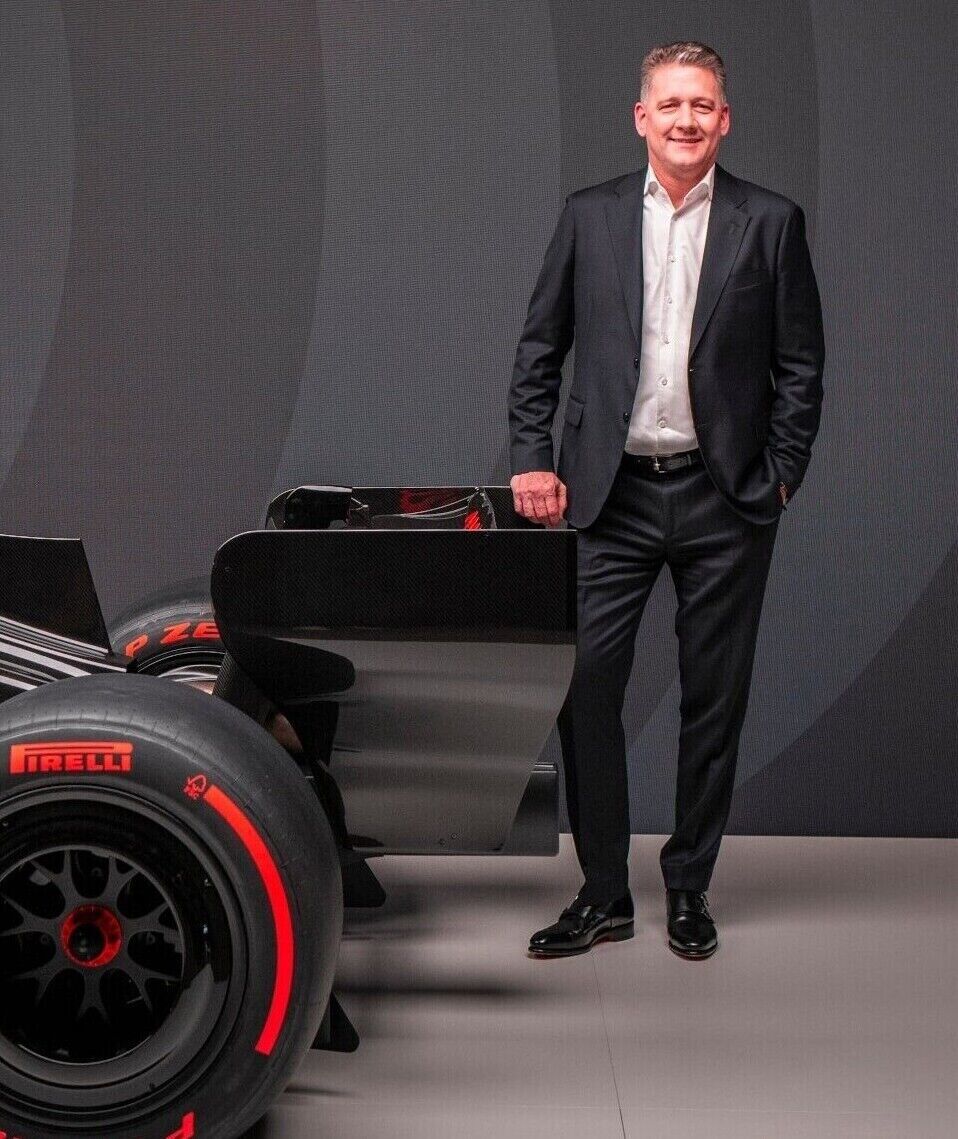 The Audi R26 Formula 1 race car with black, grey, and red racing livery and visible sponsor logos is positioned in a dark studio, with CEO Gernot Döllner standing next to it with his arms crossed.