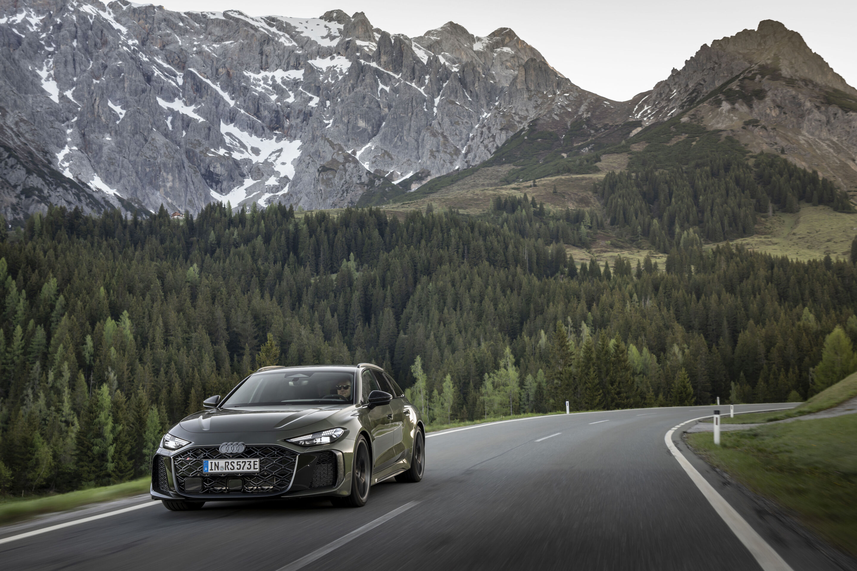 Audi RS 5 Avant - Audi RS 5 Avant in Bedfordgrün, Outdoor-Fahraufnahme, Exterieur, Dreiviertelfrontansicht auf kurviger Straße vor alpiner Bergkulisse.