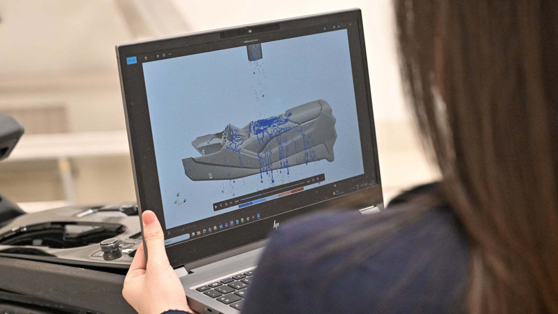 Person betrachtet auf einem Laptop die Simulation eines Wasserversuchs an einem Fahrzeugbauteil.