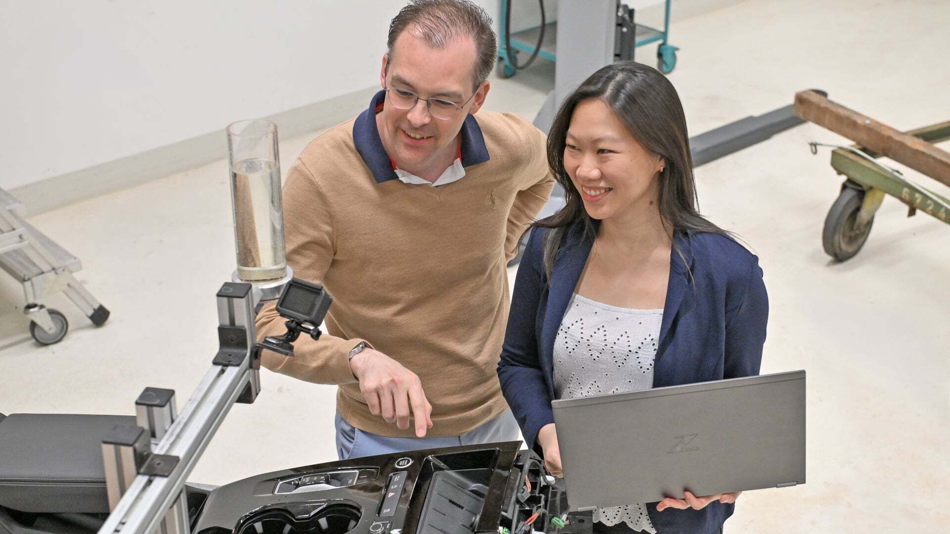 Zwei Personen betrachten mit Laptop einen Prüfaufbau an einem Fahrzeugbauteil.