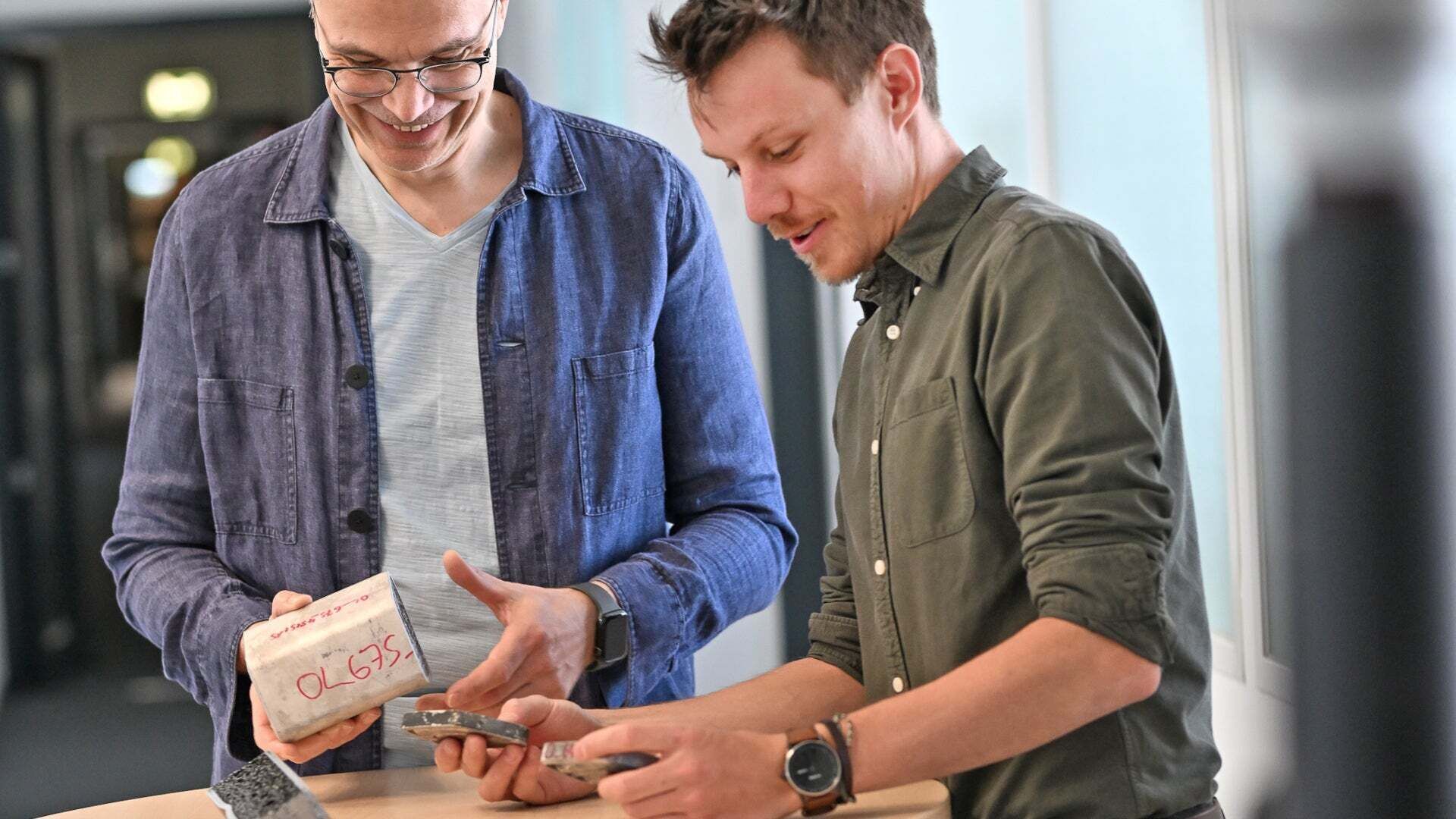 Zwei Männer betrachten Materialproben auf einem Tisch in einem Innenraum.
