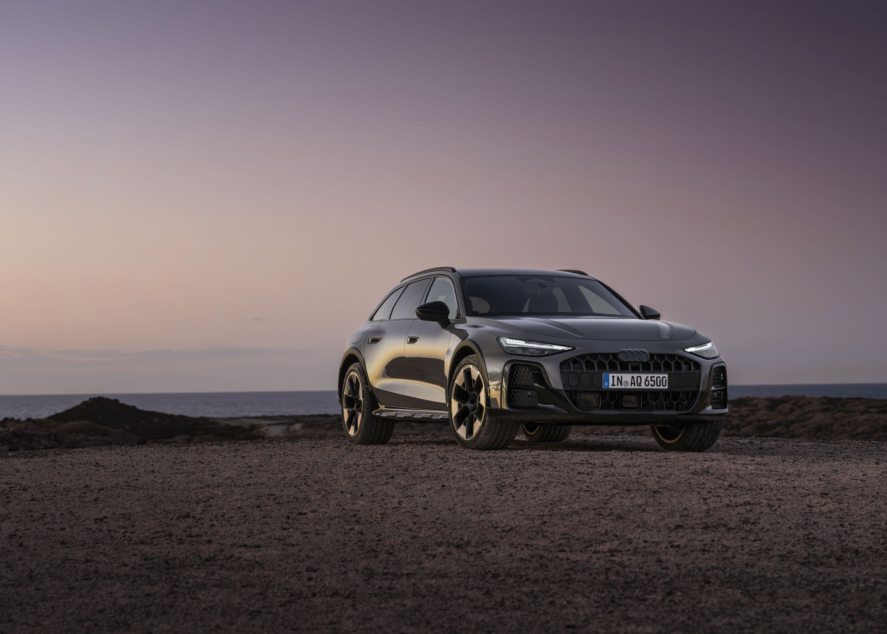 Audi A6 allroad quattro - ¾ Frontansicht des Audi A6 allroad (plateaugrau metallic) vor ruhigem Meereshorizont in der Abenddämmerung.