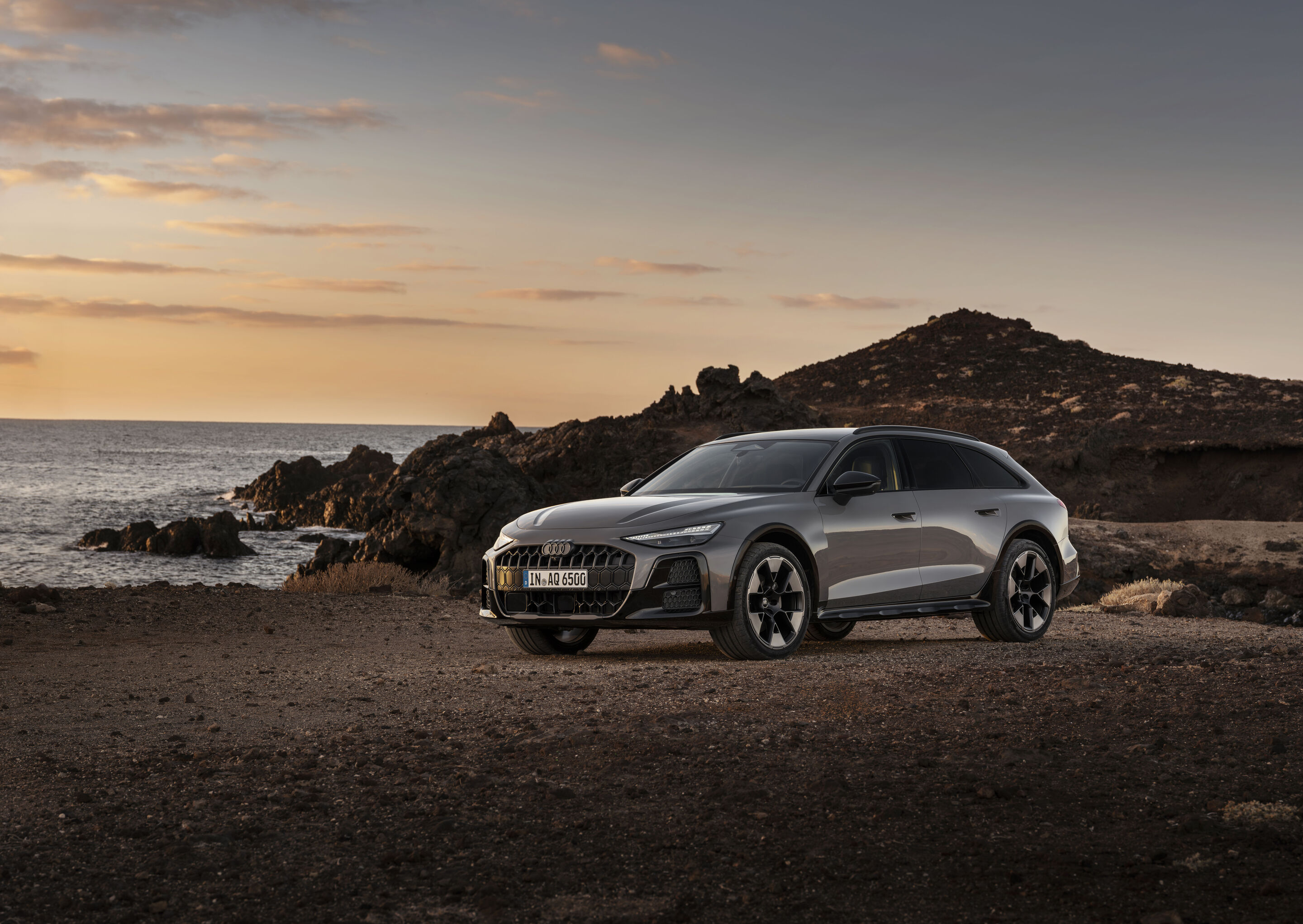 Audi A6 allroad quattro - Audi A6 allroad (plateaugrau metallic) in Seitenansicht an einer felsigen Küstenlandschaft bei Sonnenuntergang.