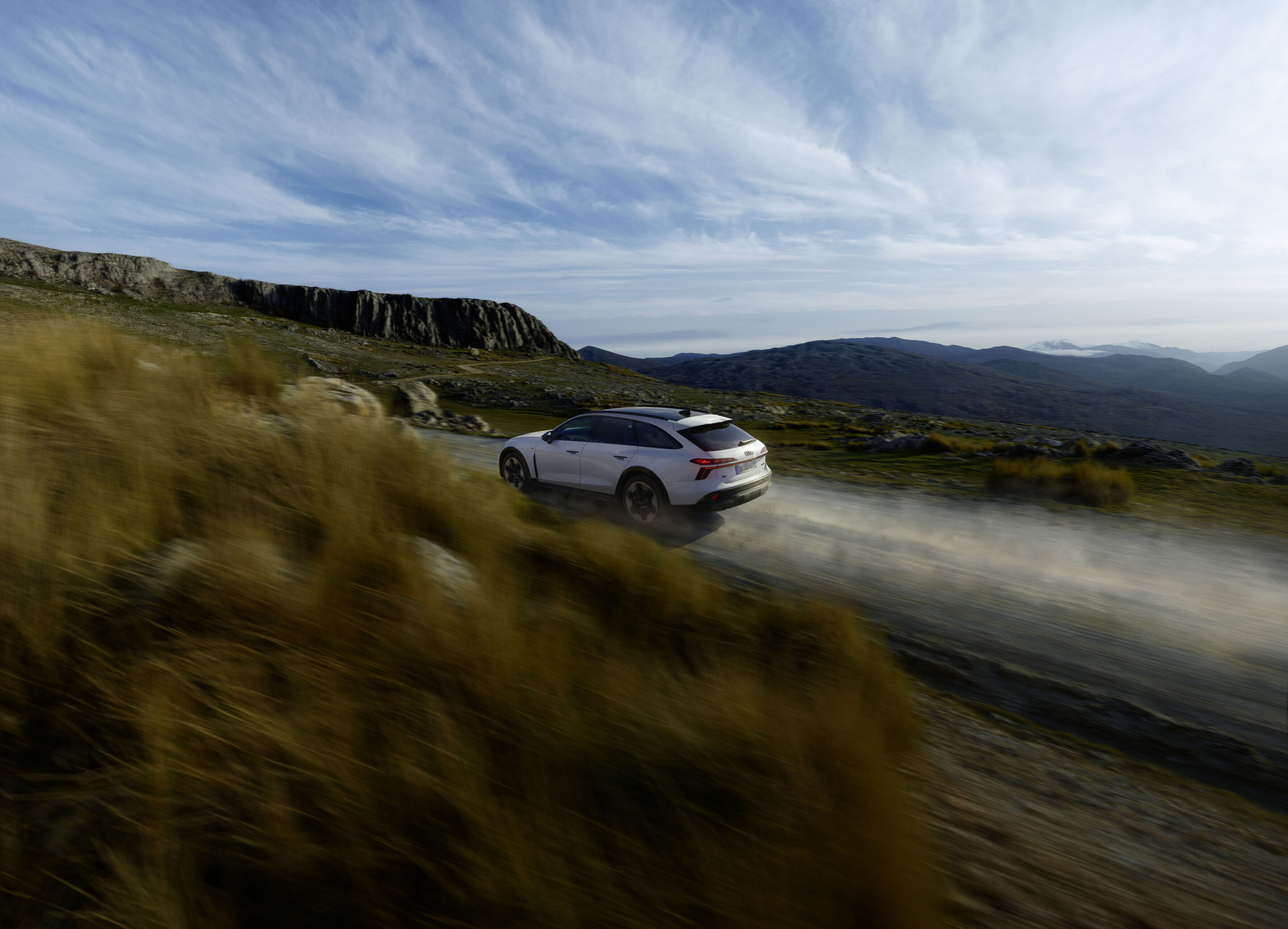 Audi A6 allroad e-hybrid quattro - Dynamische Aufnahme: Audi A6 allroad e-hybrid (gletscherweiß) auf Schotterpiste in bergiger Landschaft – dynamisch und kontrolliert auch abseits befestigter Straßen.