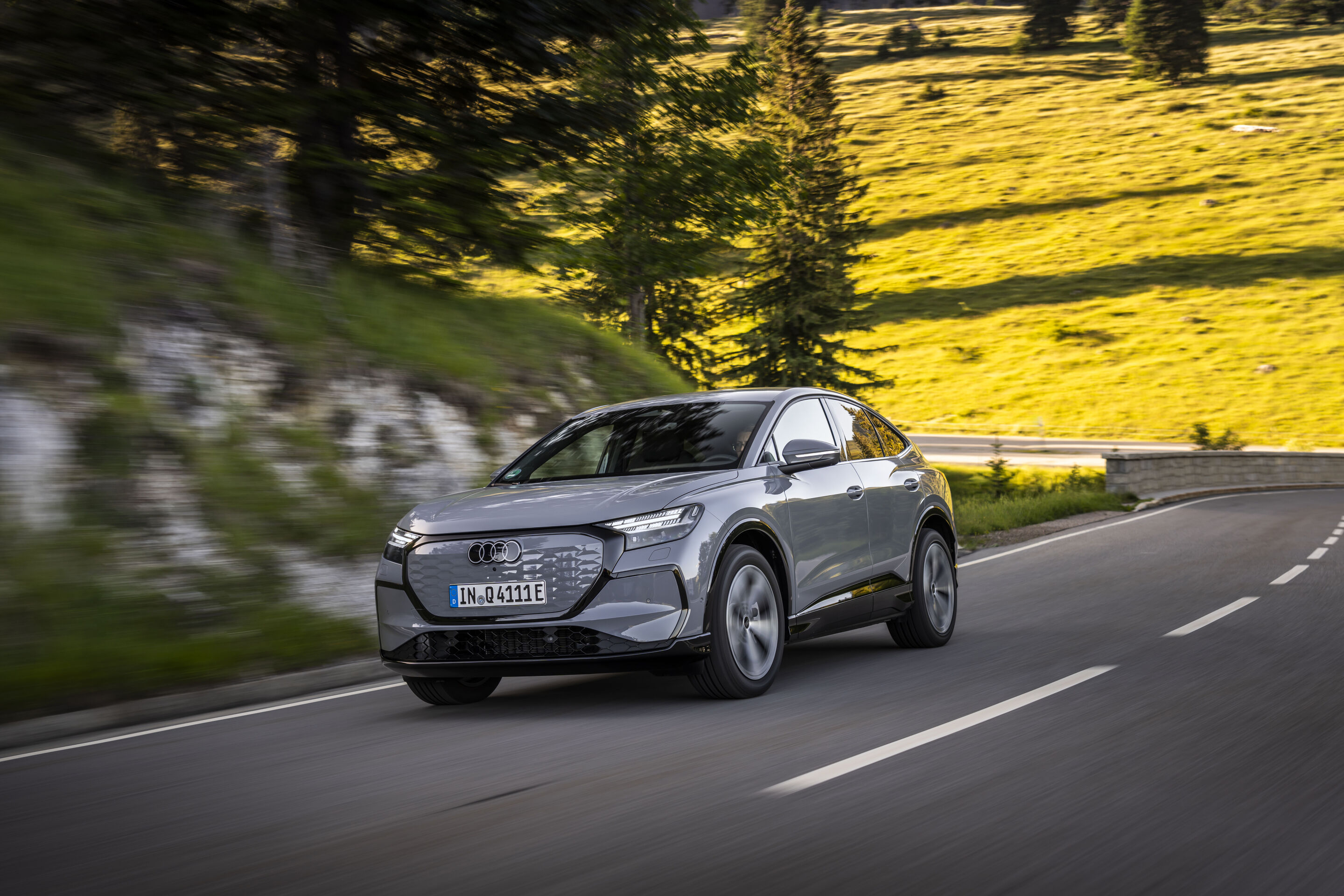 Ein Auto für jeden Moment: Unterwegs im Audi Q4 e-tron - Audi Q4 Sportback e-tron in Pebblegrau, Outdoor-Fahraufnahme, Exterieur, Dreiviertelfrontansicht auf kurviger Langstraße in bergiger Landschaft.