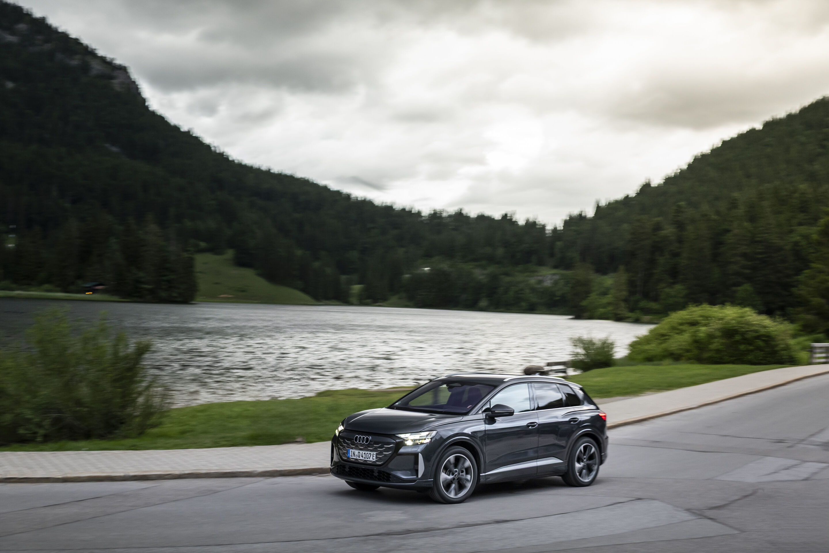Ein Auto für jeden Moment: Unterwegs im Audi Q4 e-tron - Audi Q4 SUV e-tron in Tamboragrau, Outdoor-Fahraufnahme, Exterieur, Seitenansicht entlang eines Sees.
