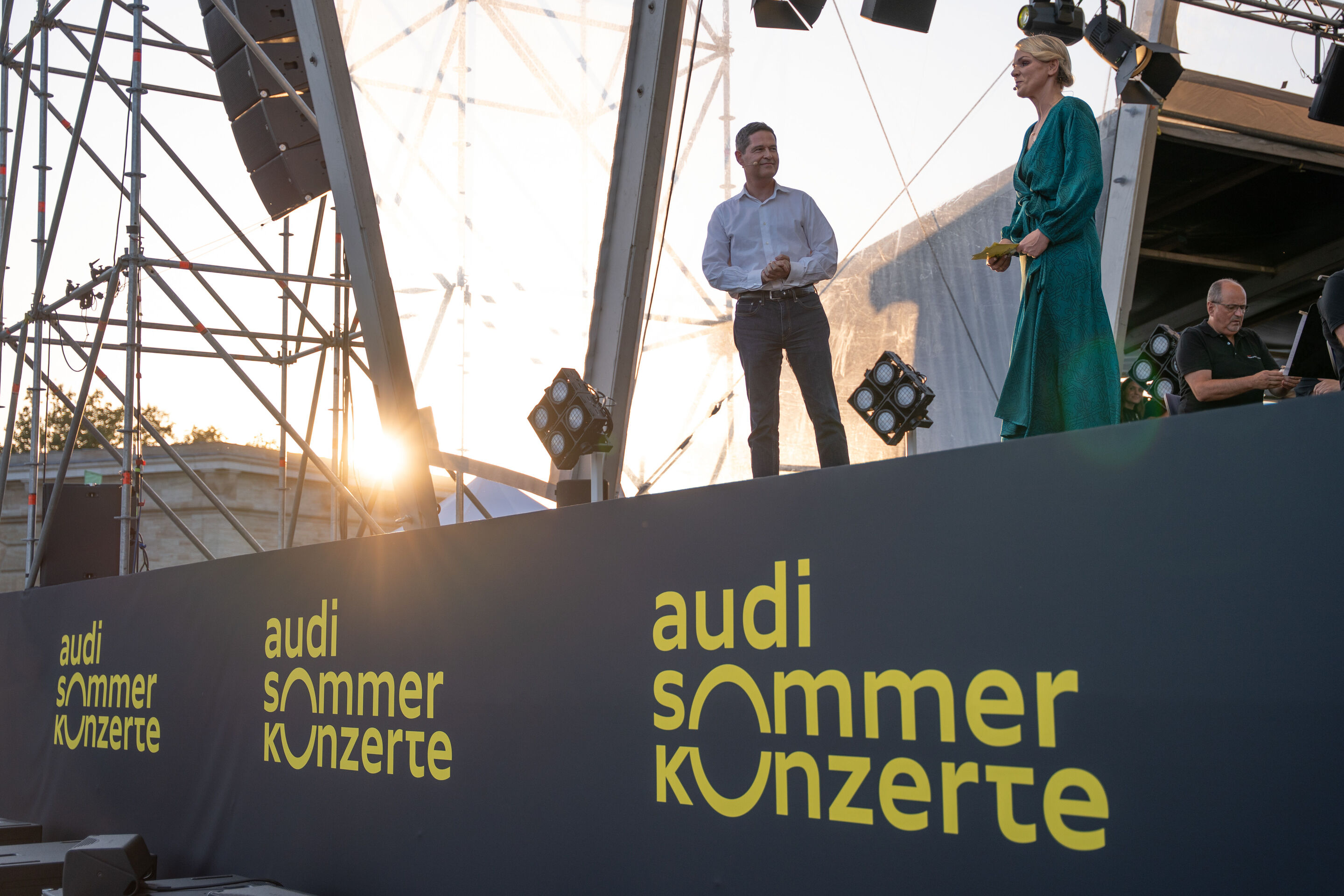 Die Audi Bläserphilharmonie beim Eröffnungskonzert/Klassik Open Air im Klenzepark - Beim Klassik Open Air 2026 im Klenzepark mit der Audi Bläserphilharmonie im Rahmen der Audi Sommerkonzerte begrüßen Xavier Ros, Mitglied des Vorstands Personal, und Moderatorin...