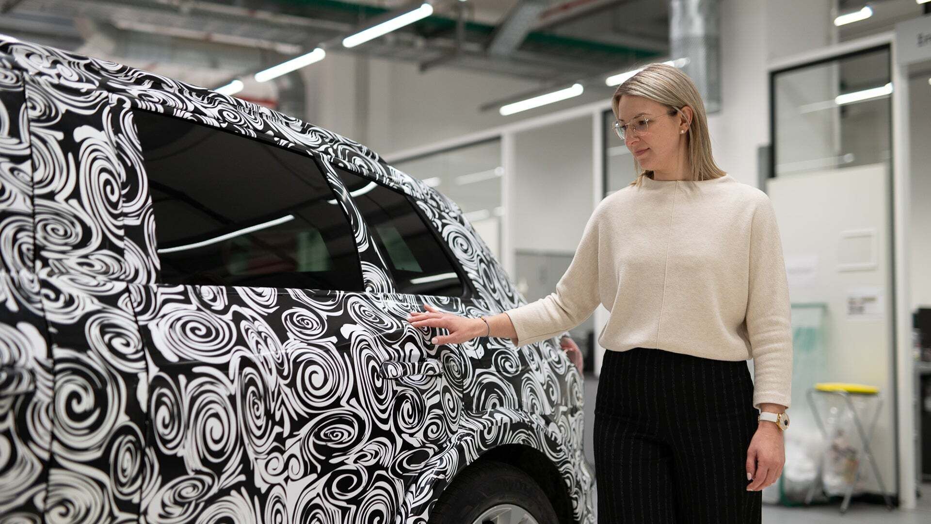 Raphaela Fritz - Raphaela Fritz fasst mit der rechten Hand einen folierten Audi in einer Werkstatt an