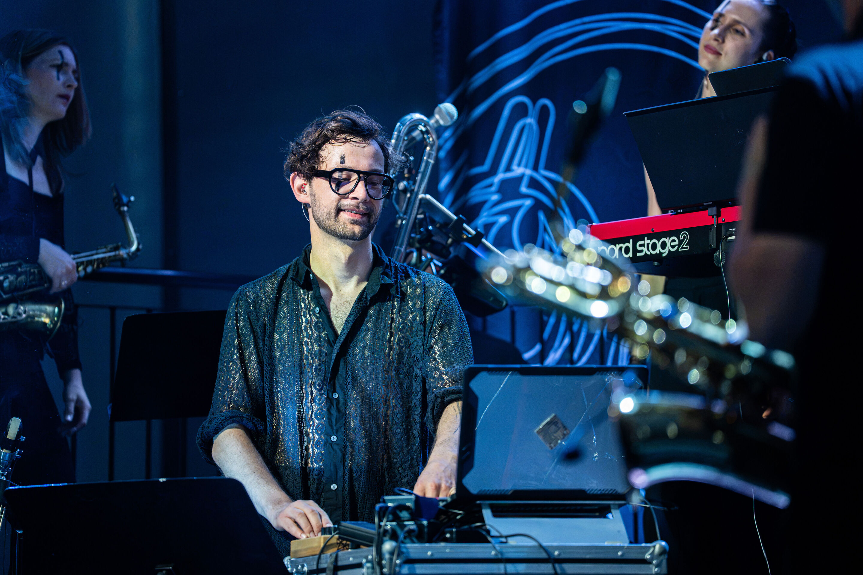 Audi Summer concert: Jazzrausch Bigband performing “Verdi’s Breakdown” - Composer Leonhard Kuhn stands at an electronic mixing console on the blue-lit stage in the Audi H6 building. In the background, additional members of the Jazzrausch Bigband can be...