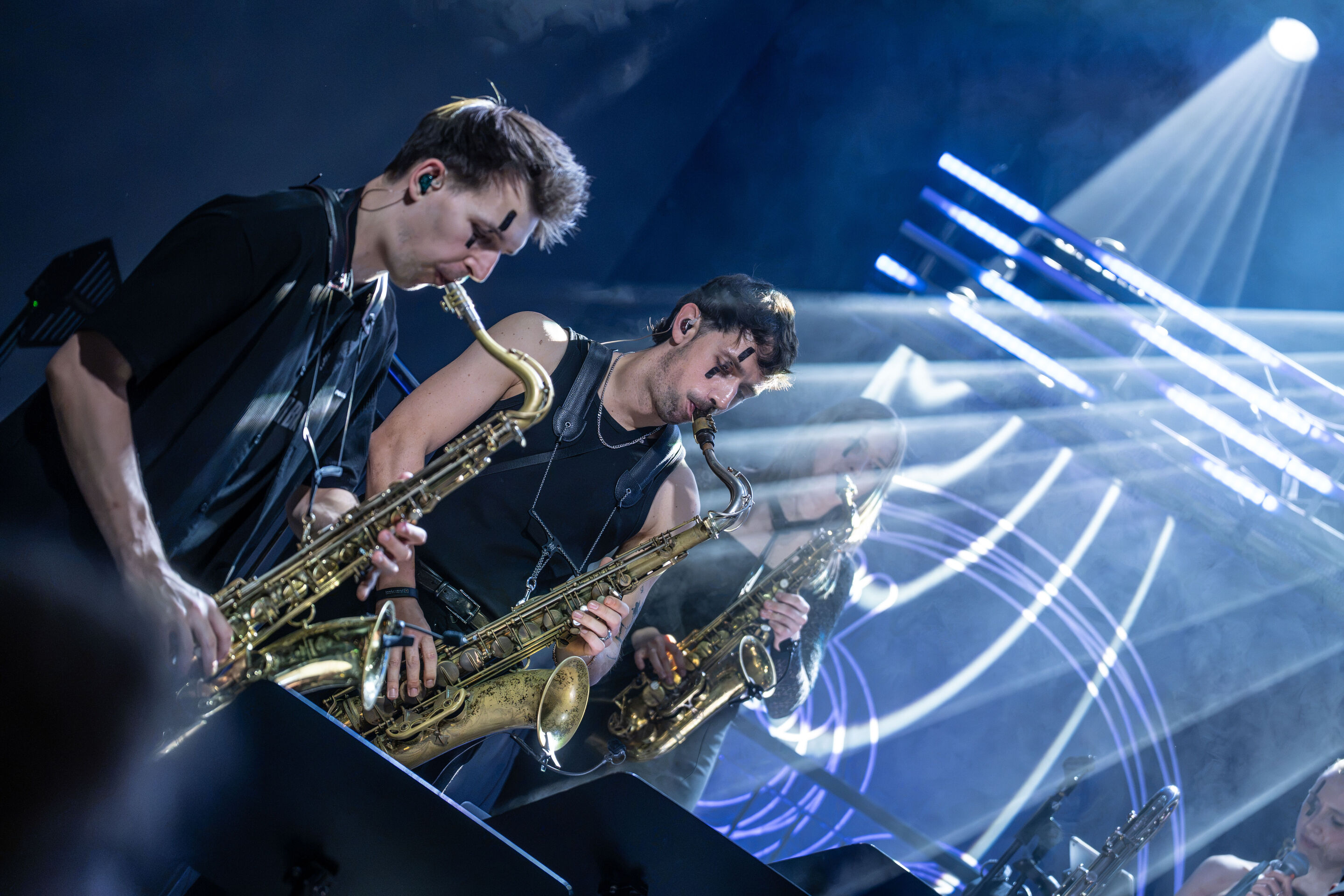 Audi Summer concert: Jazzrausch Bigband performing “Verdi’s Breakdown” - Three saxophonists from the Jazzrausch Bigband perform on the blue-lit stage in the Audi H6 building. Bright beams of light sweep across the stage, while the ensemble’s vocalist...
