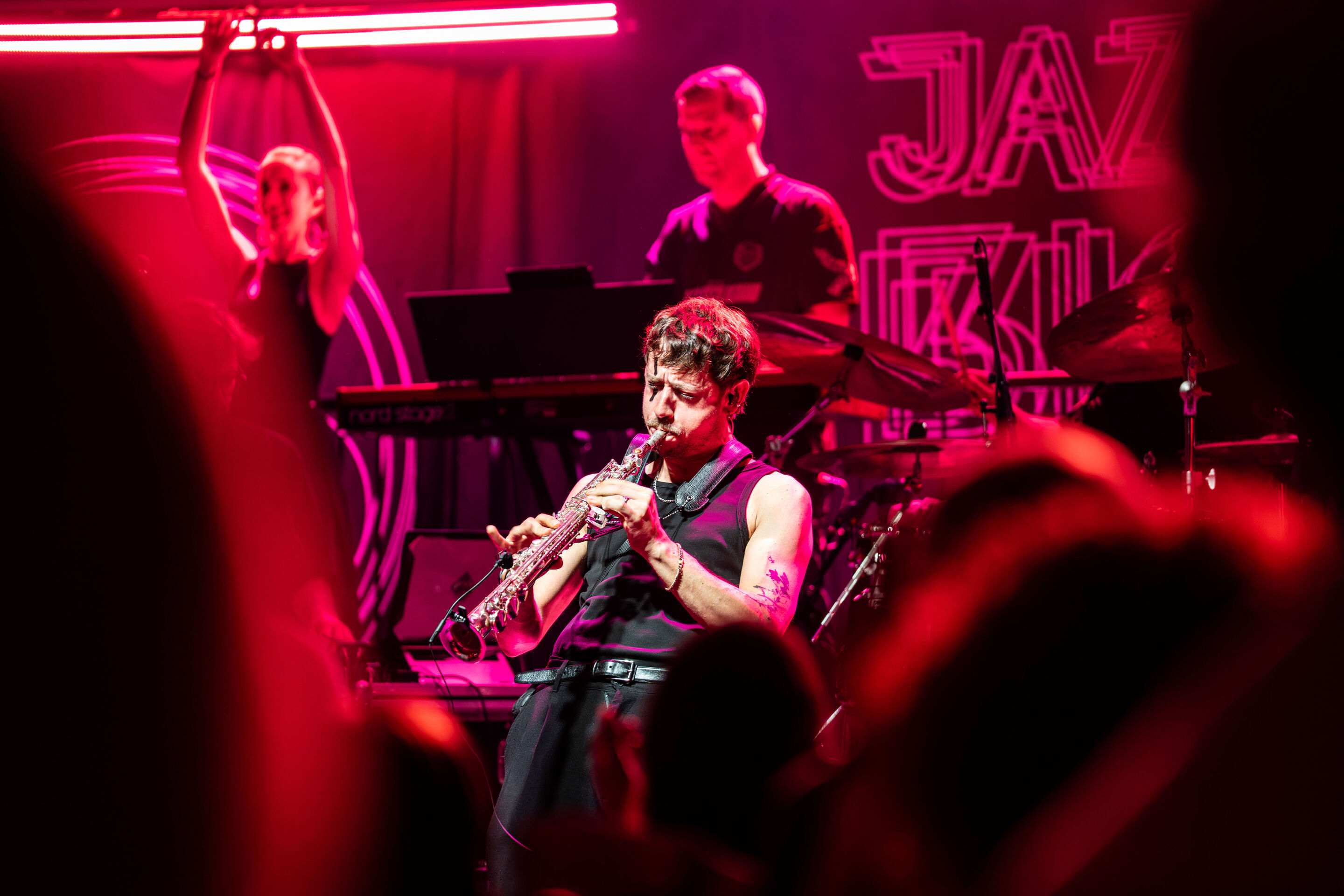 Audi Summer concert: Jazzrausch Bigband performing “Verdi’s Breakdown” - A member of the Jazzrausch Bigband plays the soprano saxophone on the pink-lit stage in the Audi H6 building. In the background, additional members of the ensemble and parts of the...