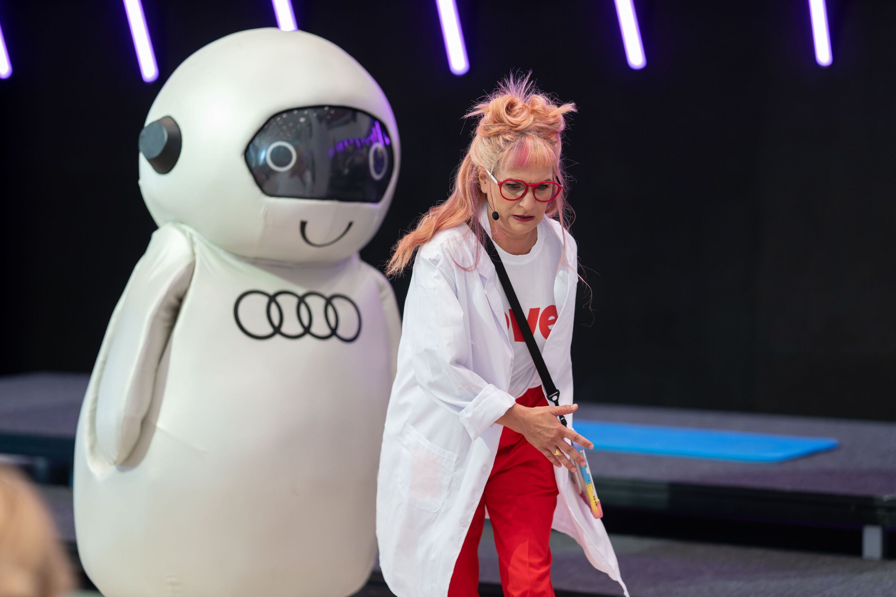 Audi Summer concert: Children’s concert “ADUI und der Geschichtenzauber” - Actress Olivia Wendt and the character ADUI stand in front of the stage in the Audi H6 building.