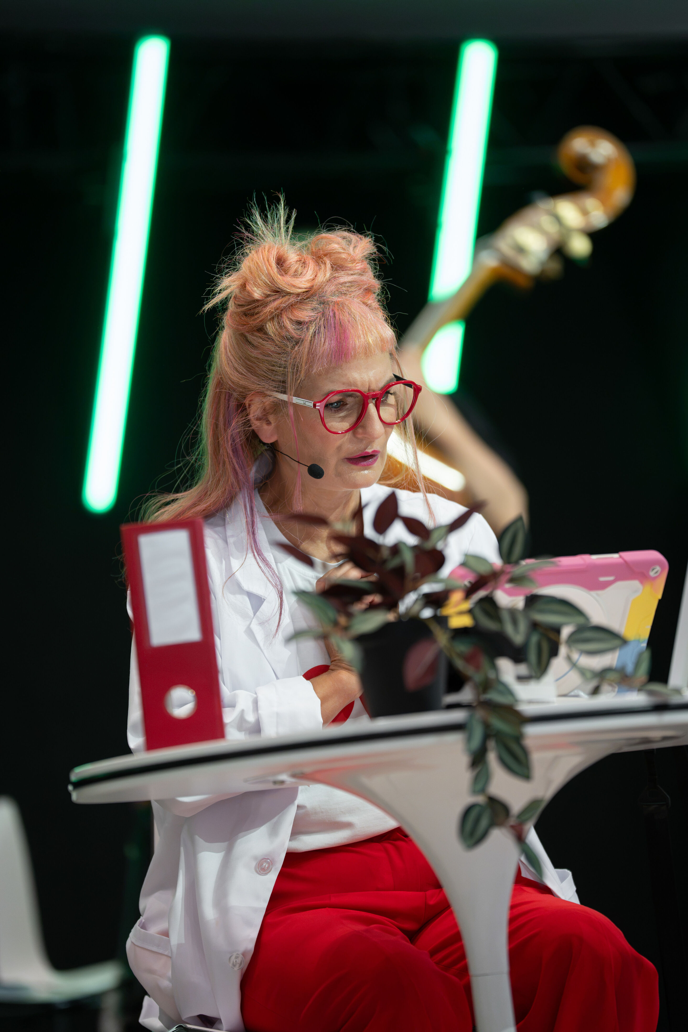 Audi Summer concert: Children’s concert “ADUI und der Geschichtenzauber” - Actress Olivia Wendt sits at a table on the stage in the Audi H6 building and looks at a tablet placed in front of her.