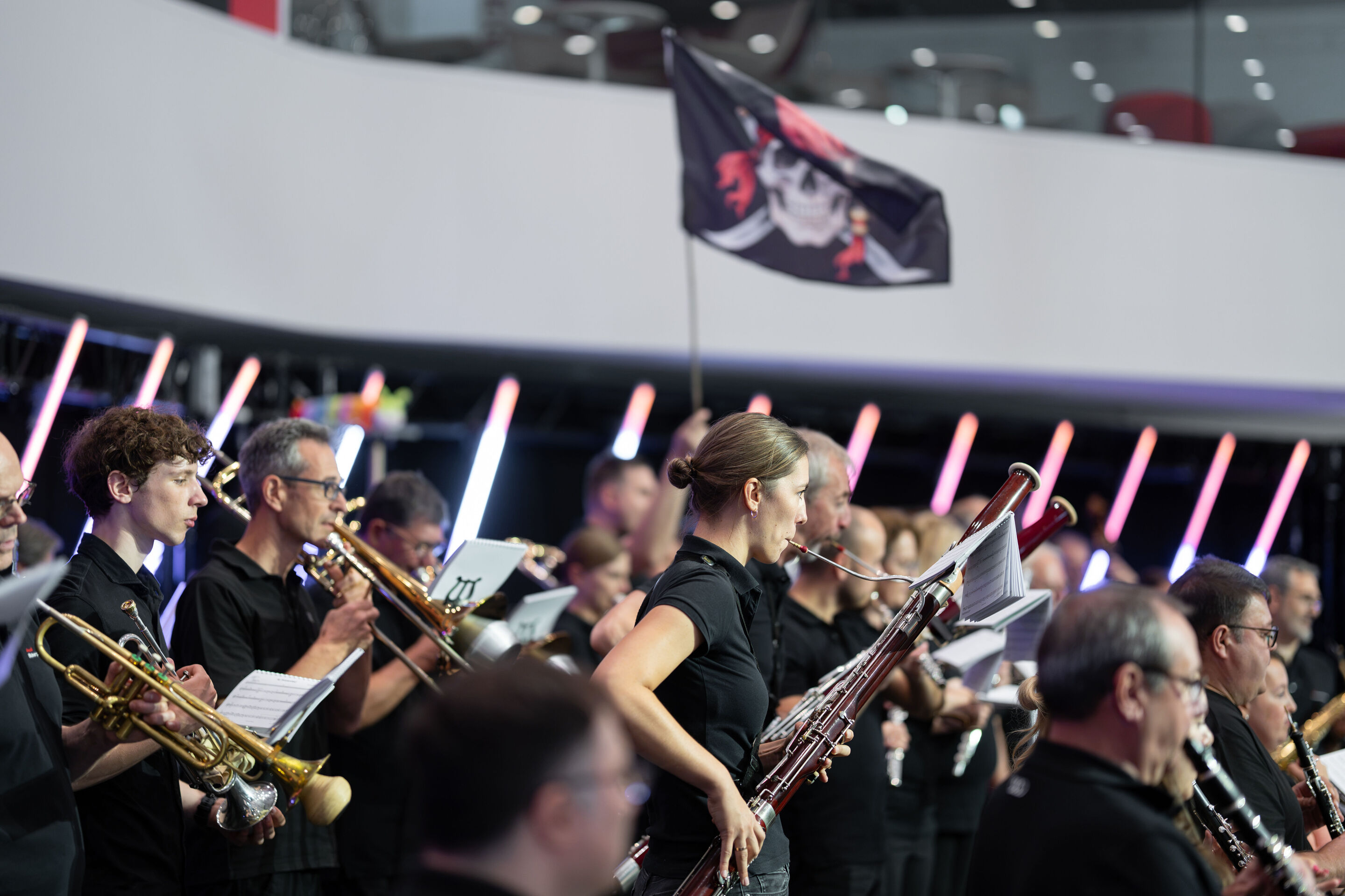 Audi Summer concert: Children’s concert “ADUI und der Geschichtenzauber” - The Audi Bläserphilharmonie performs on the stage in the Audi H6 building. In the background, a pirate flag is being held up.