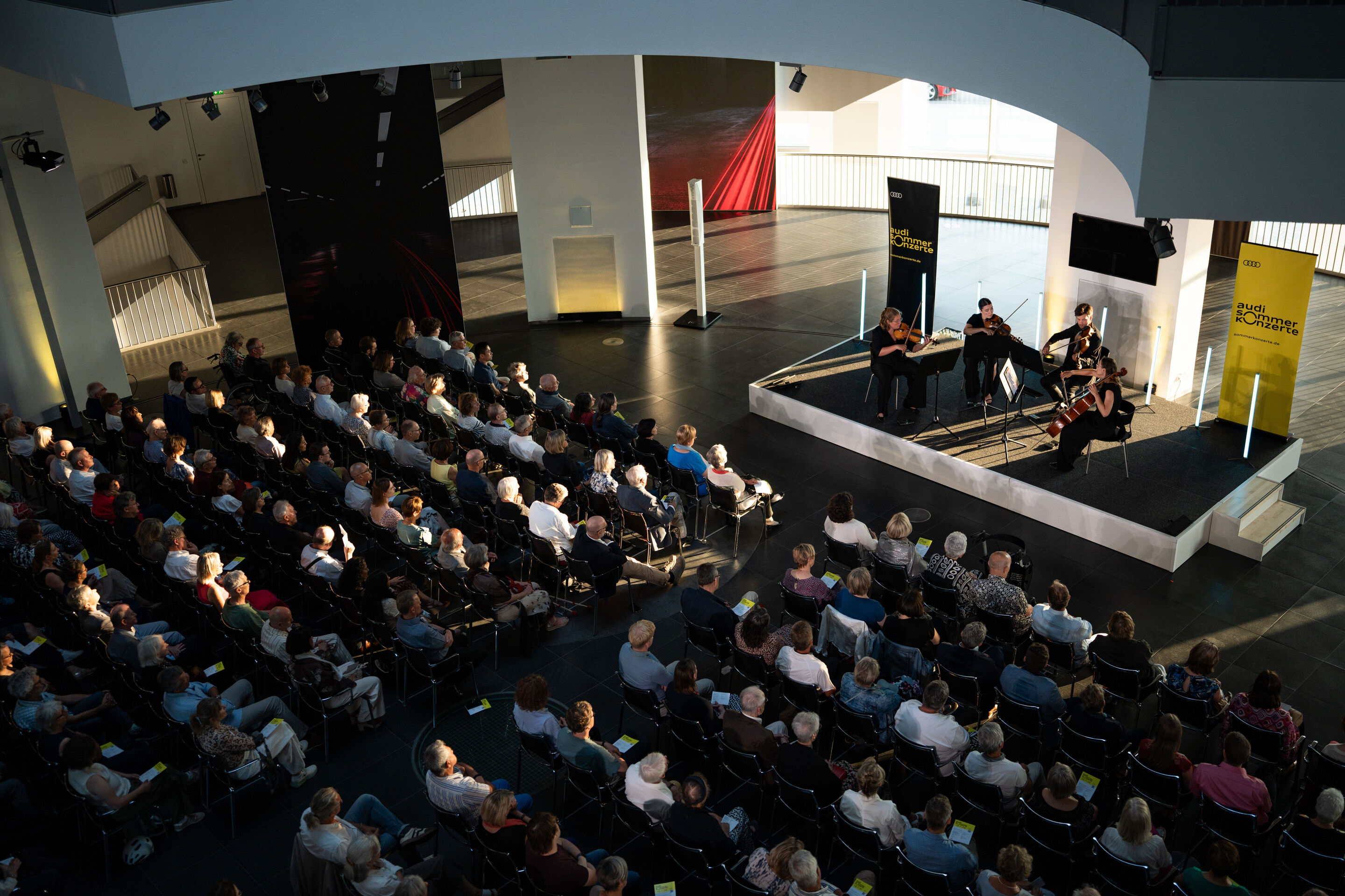 Audi Summer concert: Barbican Quartet at Audi museum mobile - View from an elevated position of the Barbican Quartet concert at the museum mobile of the Audi Forum Ingolstadt. The four musicians perform on the central stage while the audience watches...