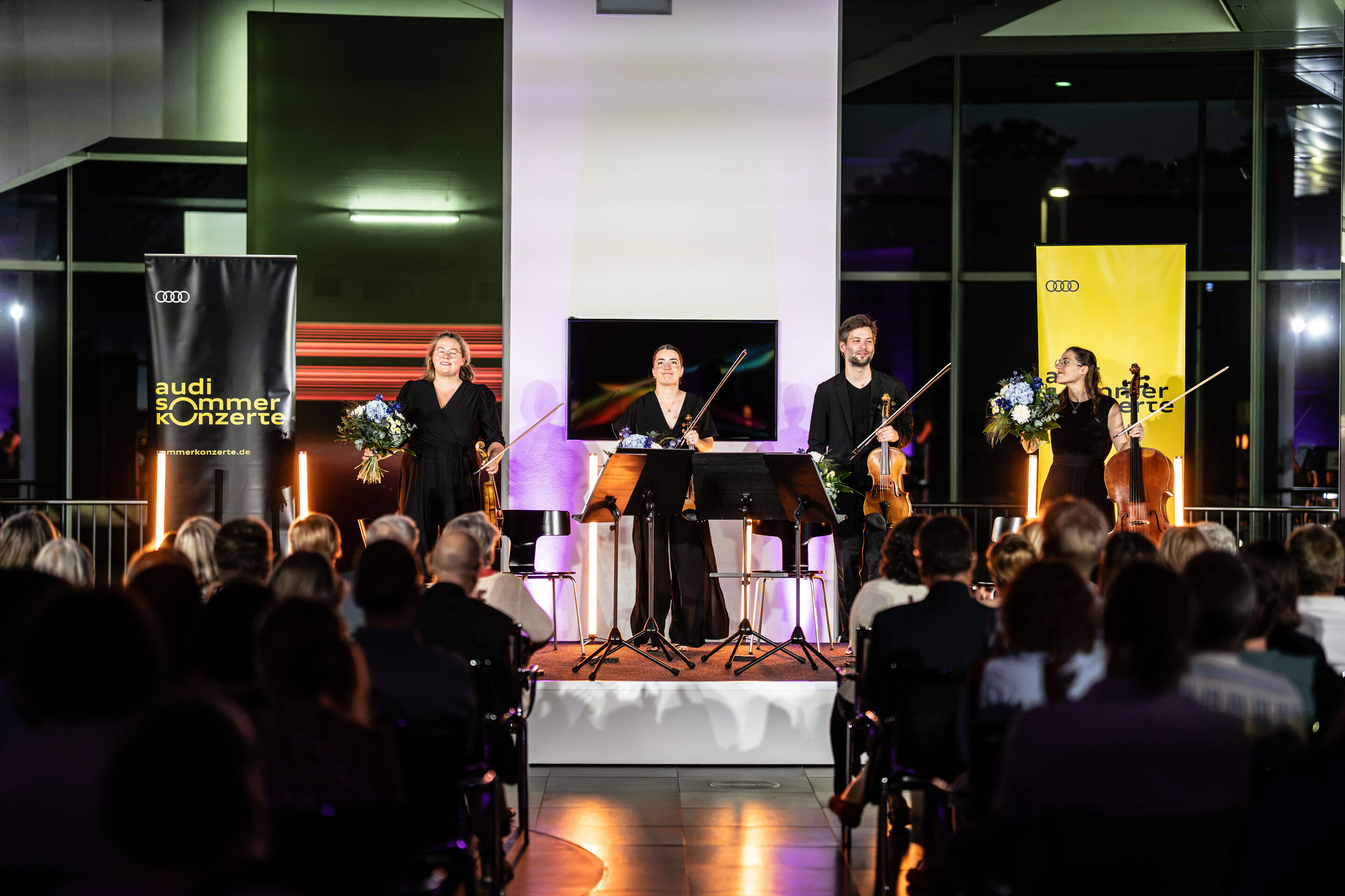 Audi Summer concert: Barbican Quartet at Audi museum mobile - View from the audience of the stage at the museum mobile of the Audi Forum Ingolstadt: The members of the Barbican Quartet stand with their string instruments in front of their music stands,...