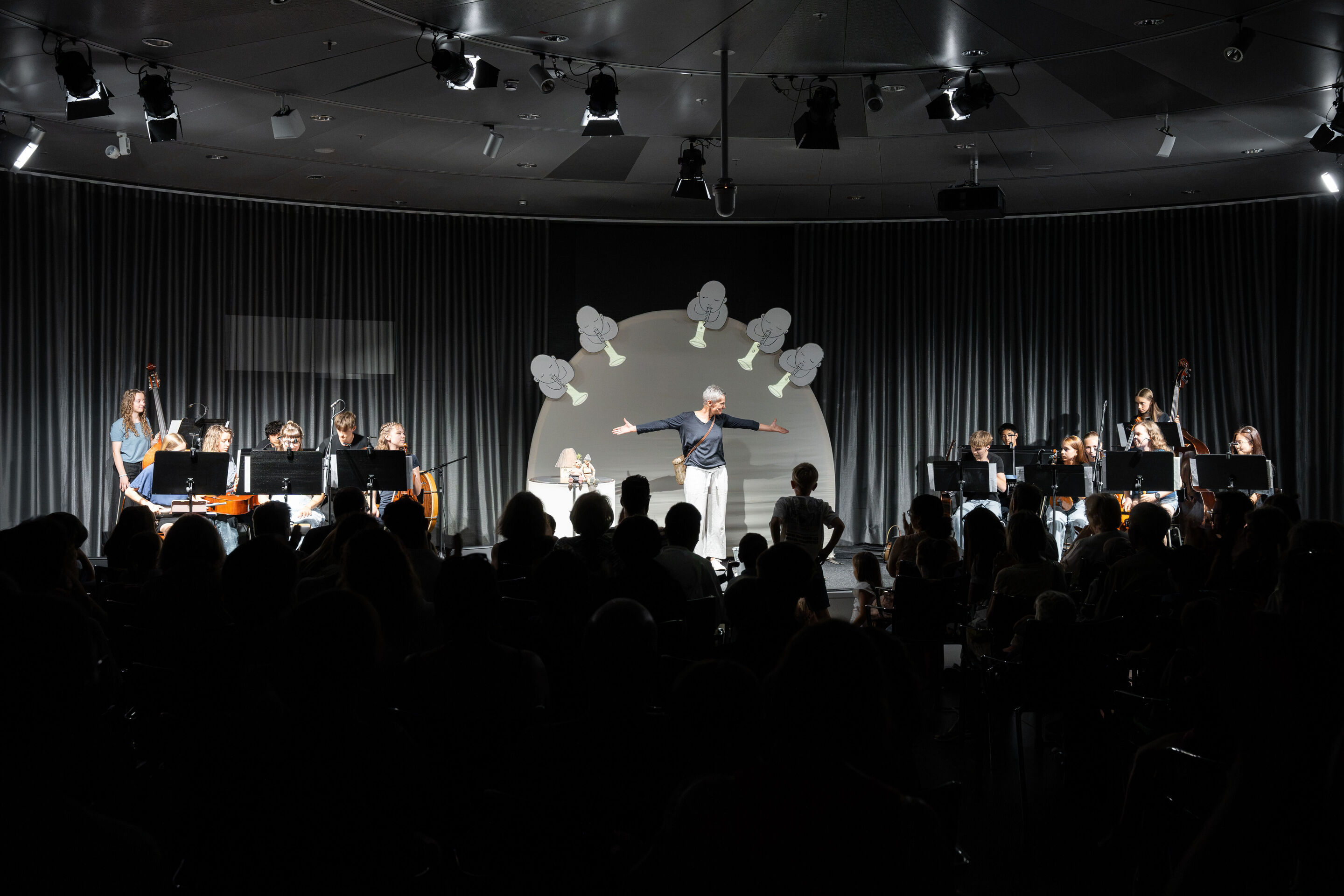 Audi Sommerkonzerte 2026 – Puppentheater „Der Fischer und seine Frau“ - Blick aus dem Publikum auf die Aufführung „Der Fischer und seine Frau“ im museum mobile des Audi Forum Ingolstadt. Annika Pilstl steht zwischen den Musikerinnen und Musikern des Ensembles...