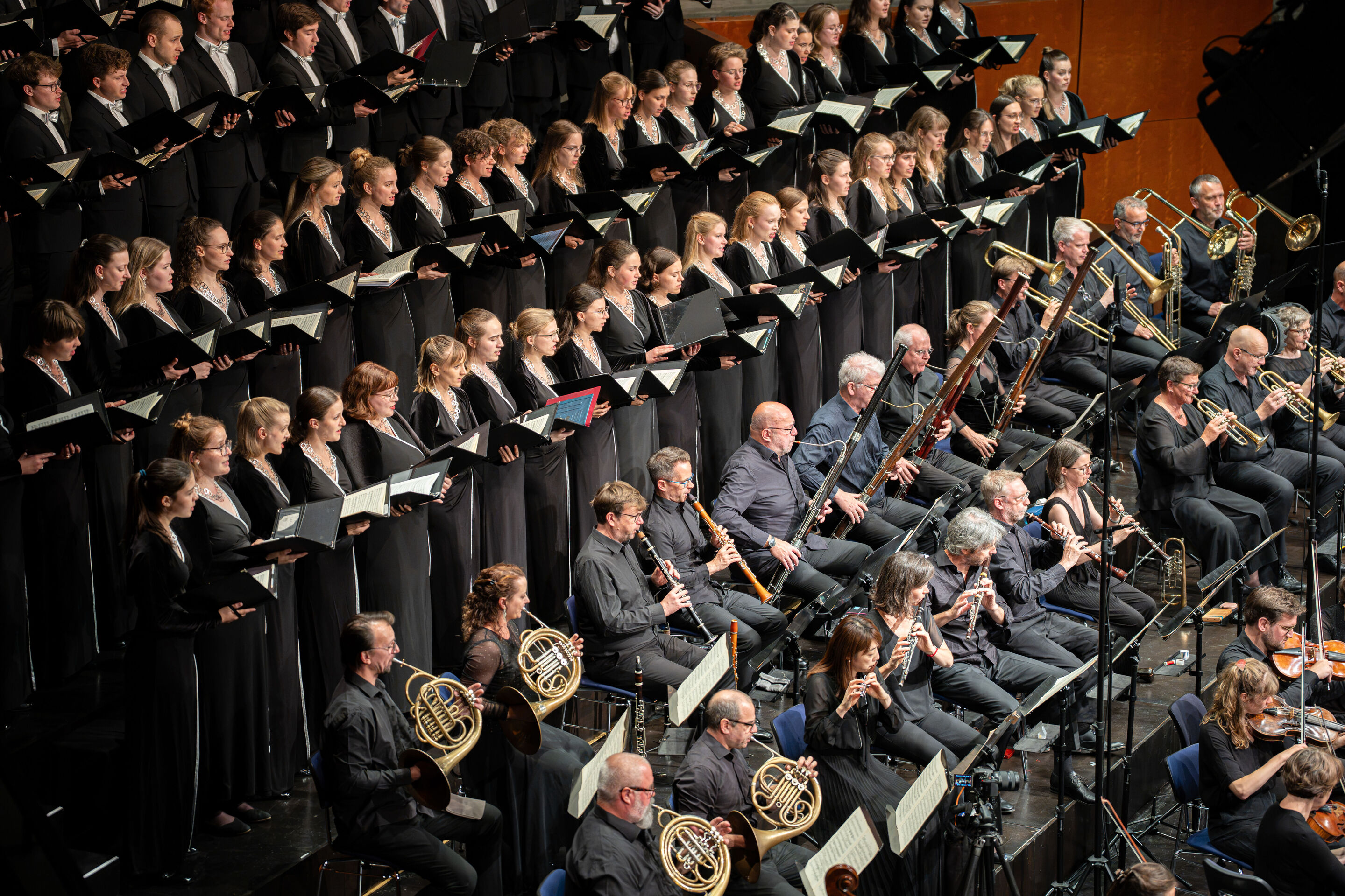 Audi Summer Concerts 2026: Closing concert - View of the stage in the Festsaal Ingolstadt from an elevated vantage point. The Audi Youth Choir Academy stands on tiered choir risers behind the Akademie für Alte Musik Berlin. Members of the orchestra perform...