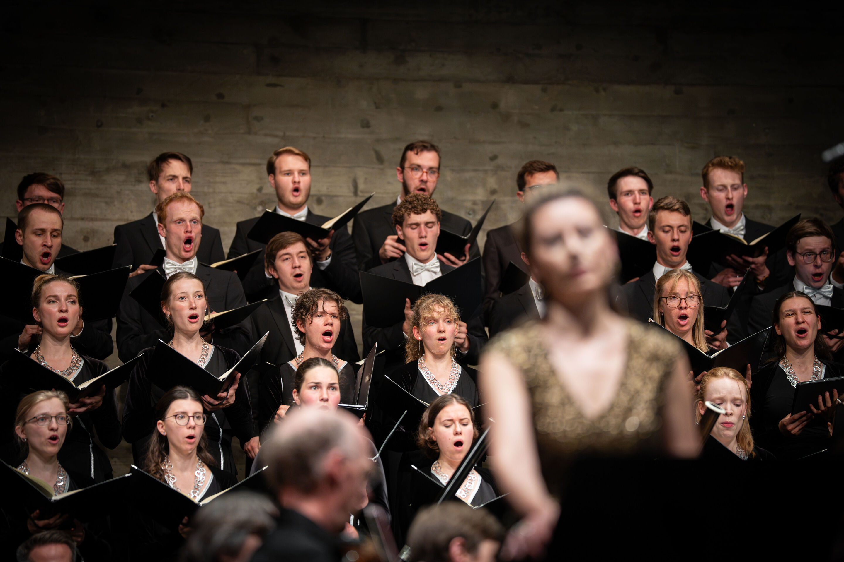 Audi Summer Concerts 2026: Closing concert - The Audi Youth Choir Academy performs on tiered choir risers in the Festsaal Ingolstadt during the performance of Verdi’s “Messa da Requiem.” In the blurred foreground, soprano Chen Reiss can be seen.