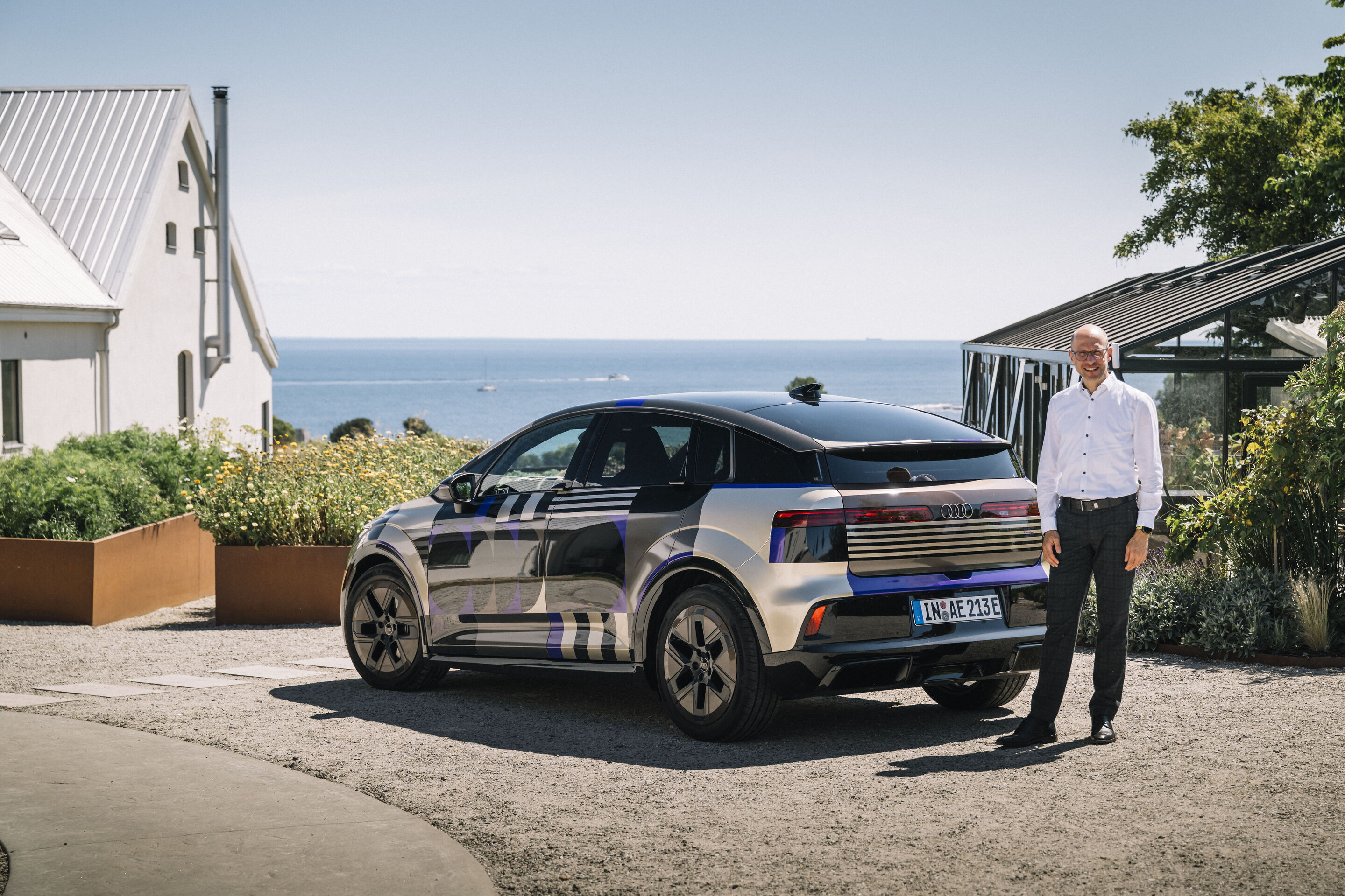 Michael Schurr in front of the Audi A2 e-tron with design livery - Technical Project Manager, stands in front of an Audi A2 e-tron with desig livery against a maritime backdrop.
